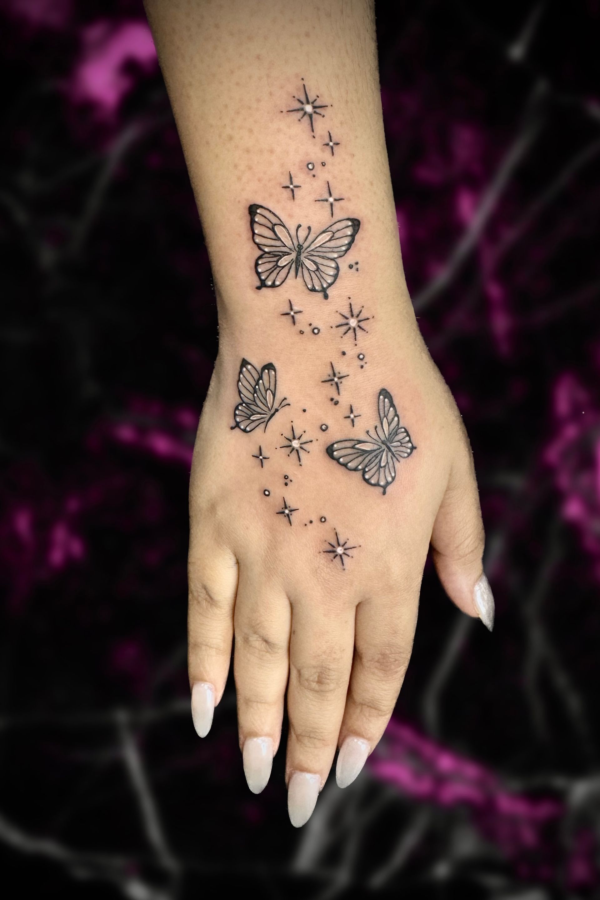 A woman has a tattoo of butterflies and stars on her hand