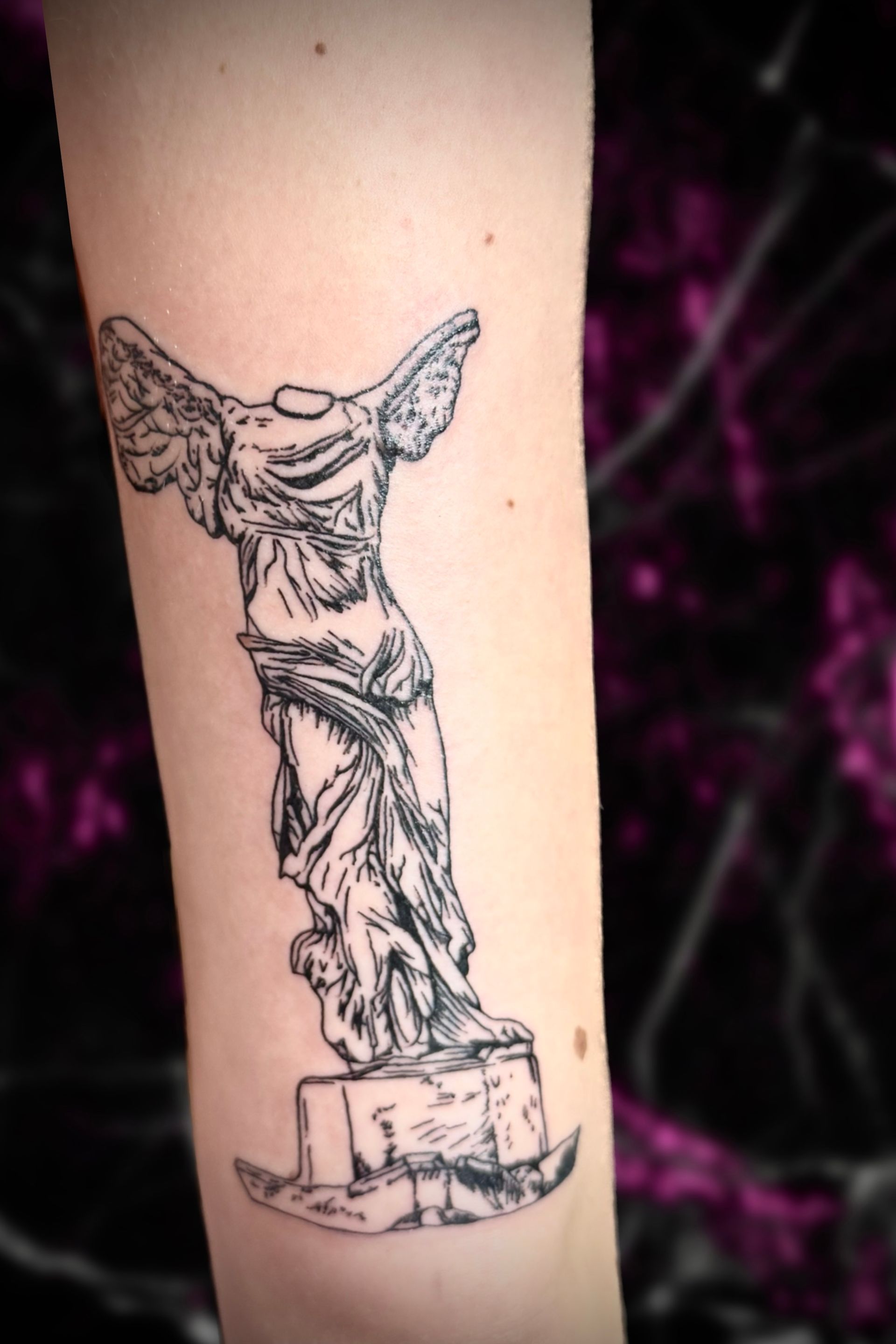 A woman has a tattoo of a statue on her arm