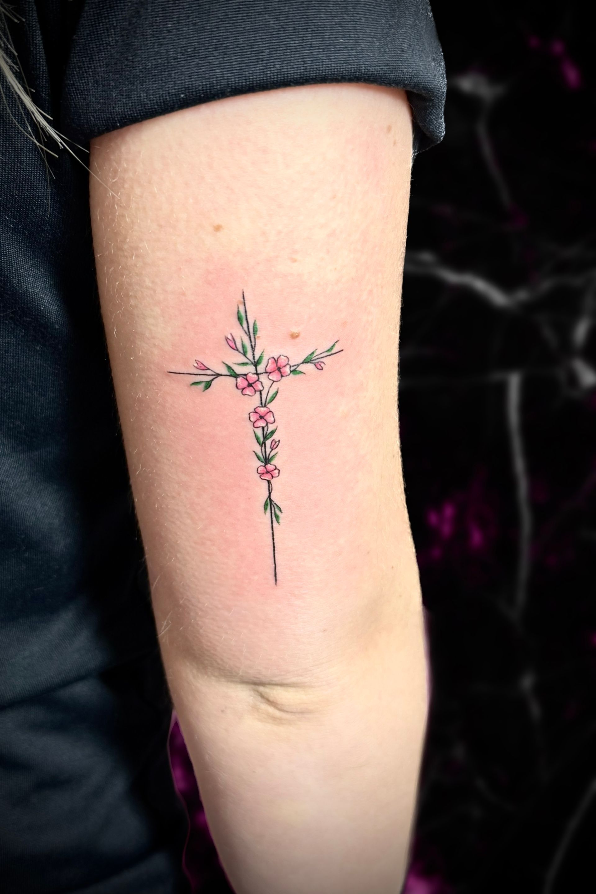 A woman has a small cross tattoo on her arm