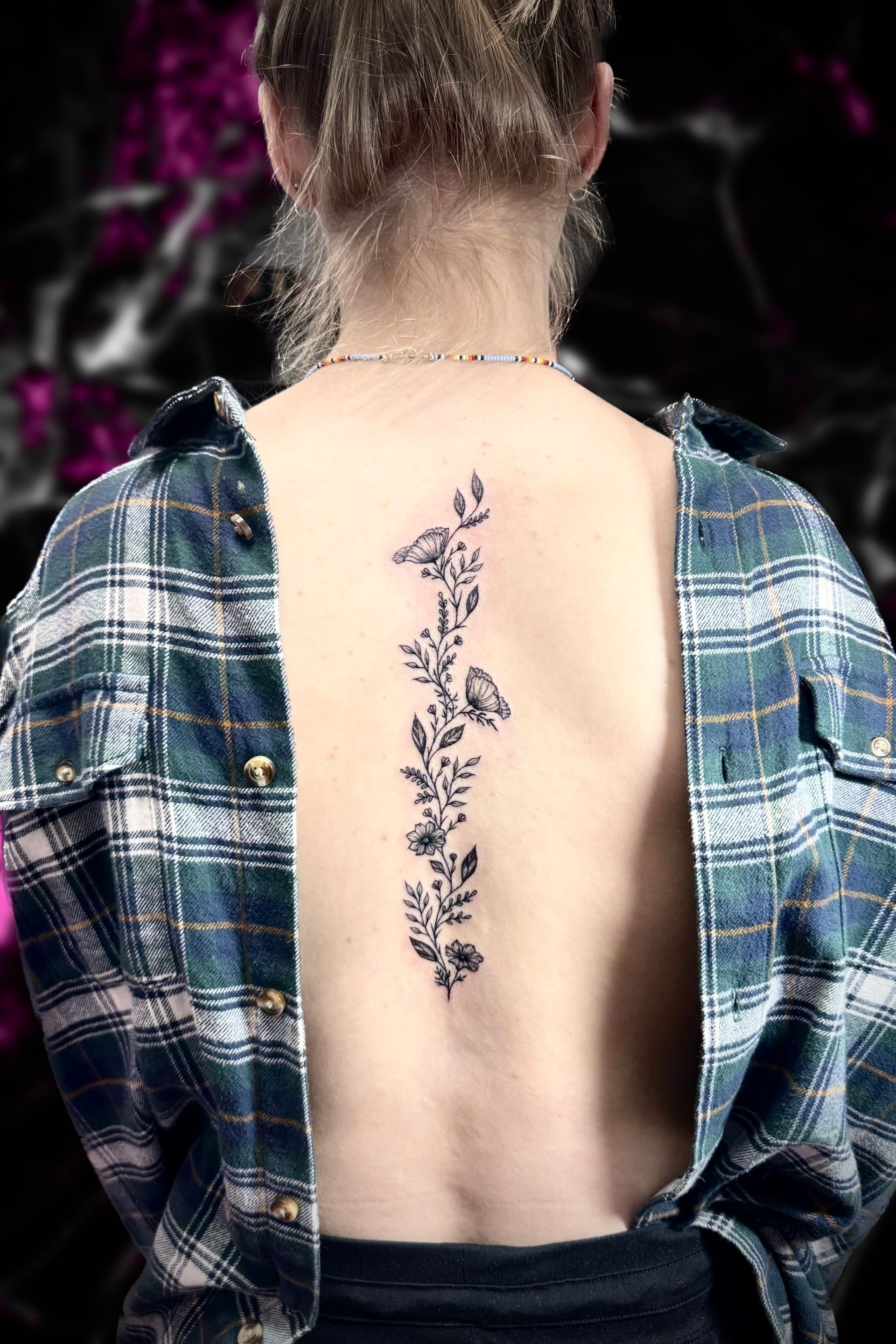 A woman with a tattoo on her back is wearing a plaid shirt