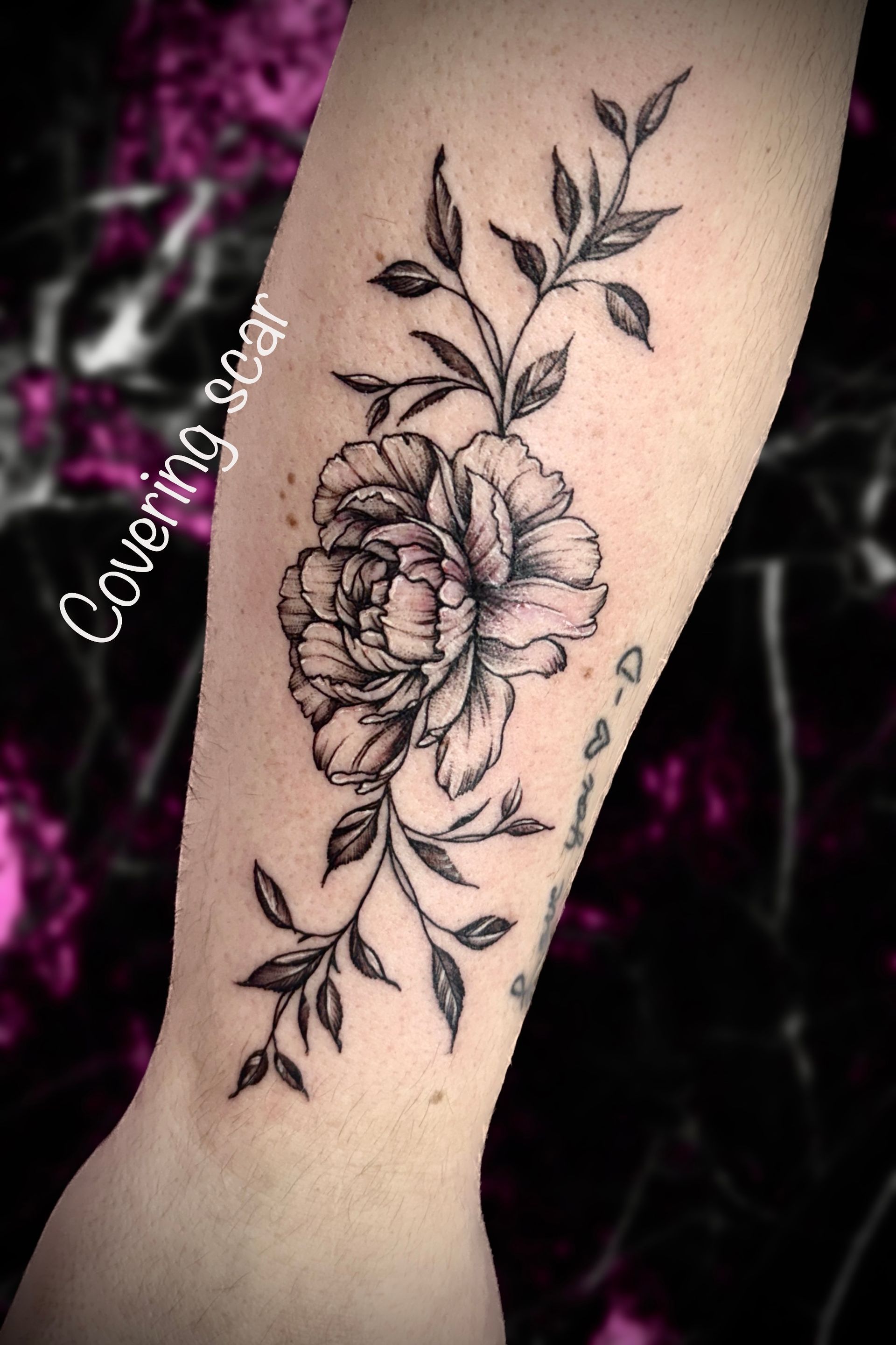A black and white tattoo of a flower and leaves on a womans forearm