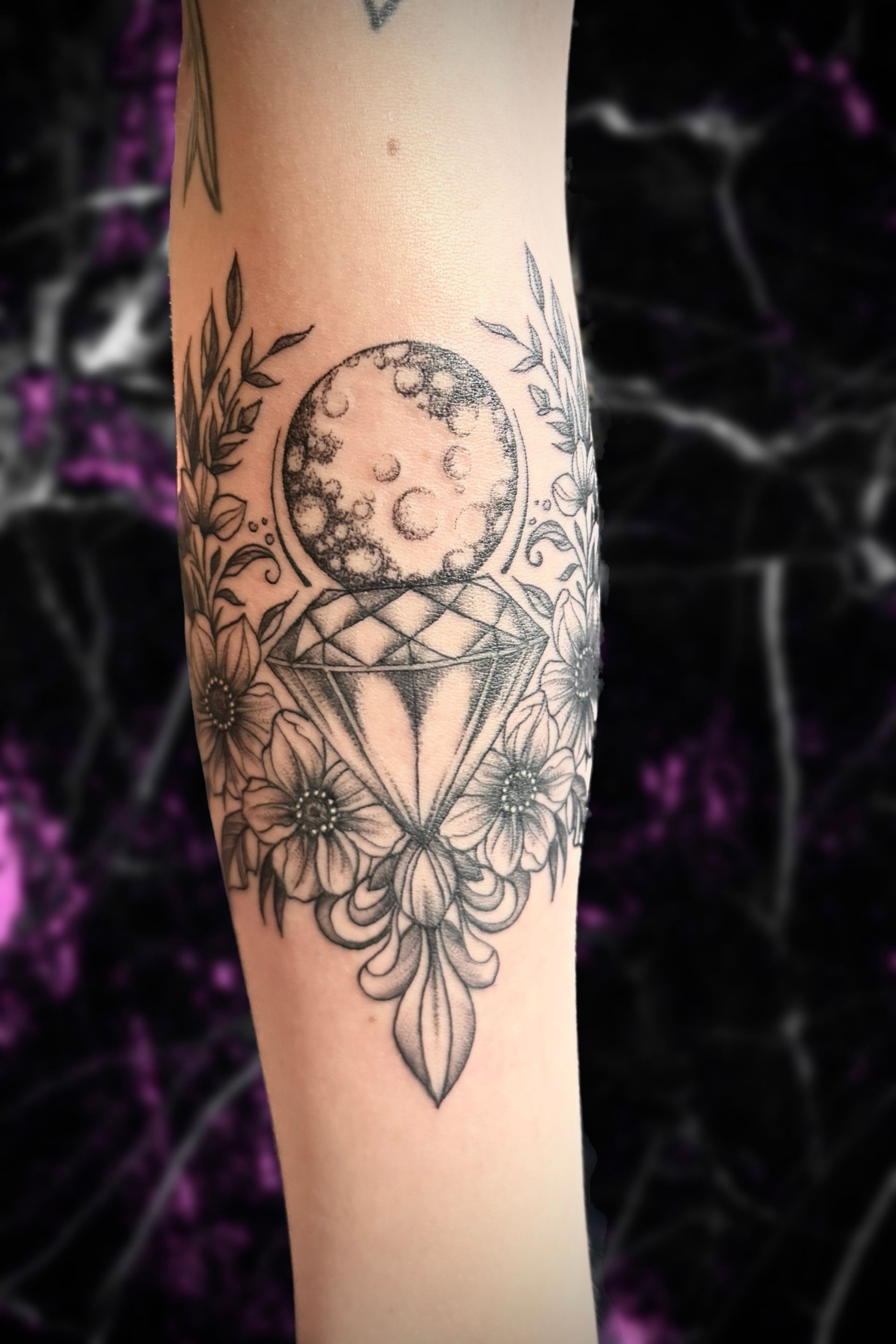 A woman has a tattoo of a crescent moon and flowers on her forearm