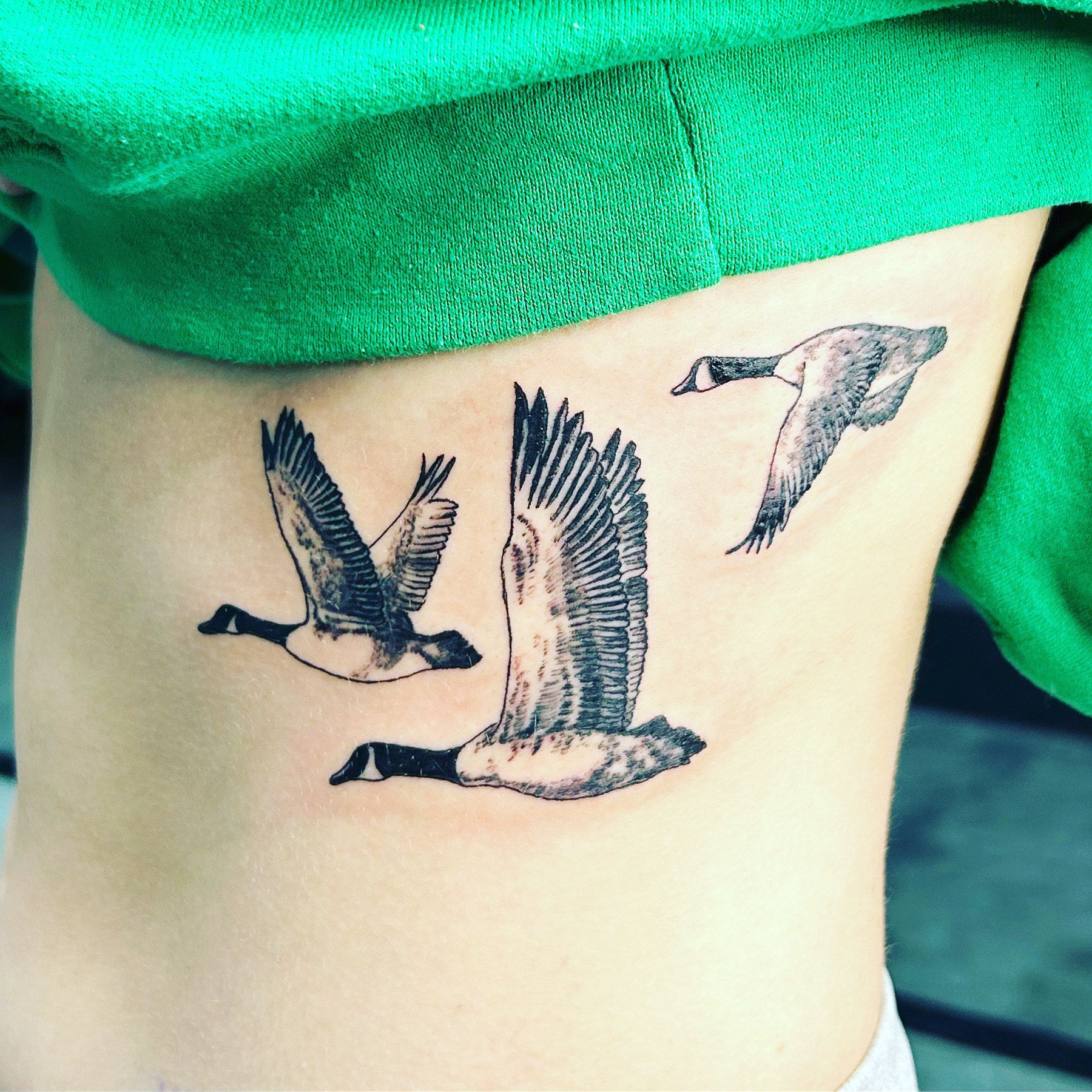 A person has a tattoo of three geese on their side