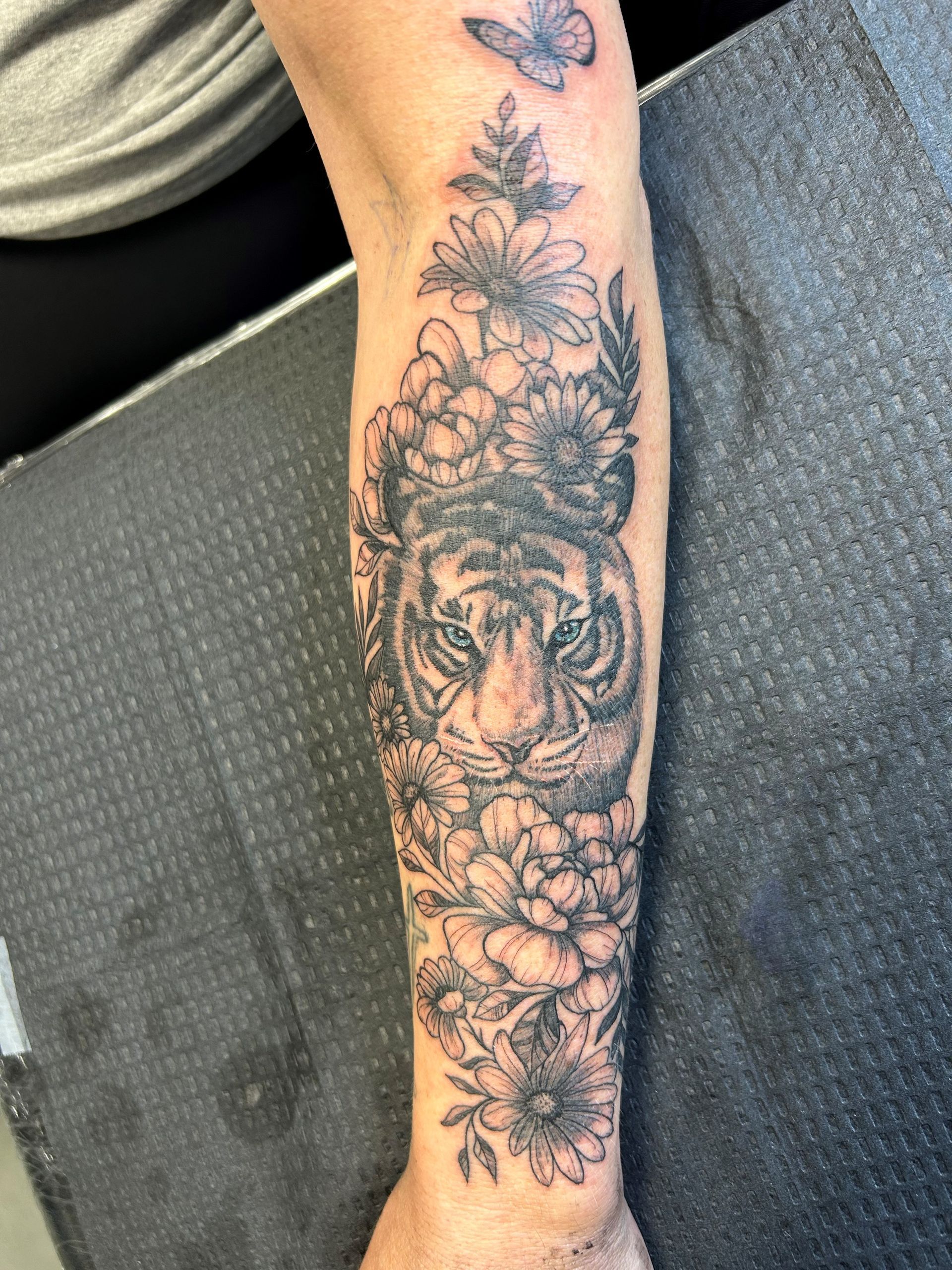 A woman has a tattoo of a tiger and flowers on her forearm.