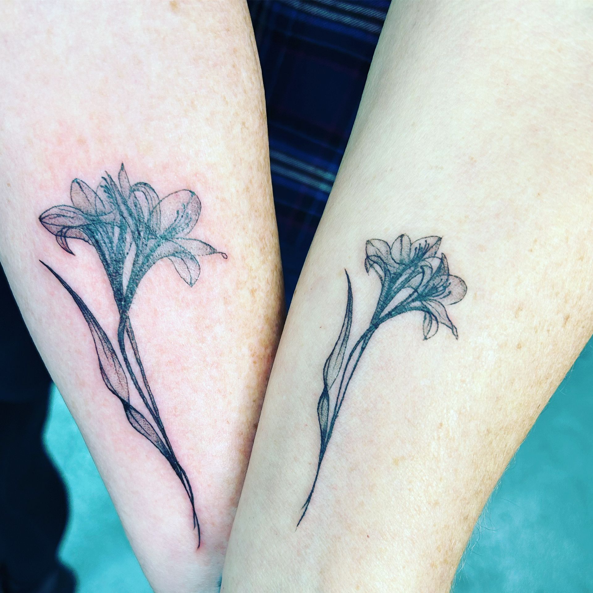 Two people have matching tattoos of flowers on their forearms