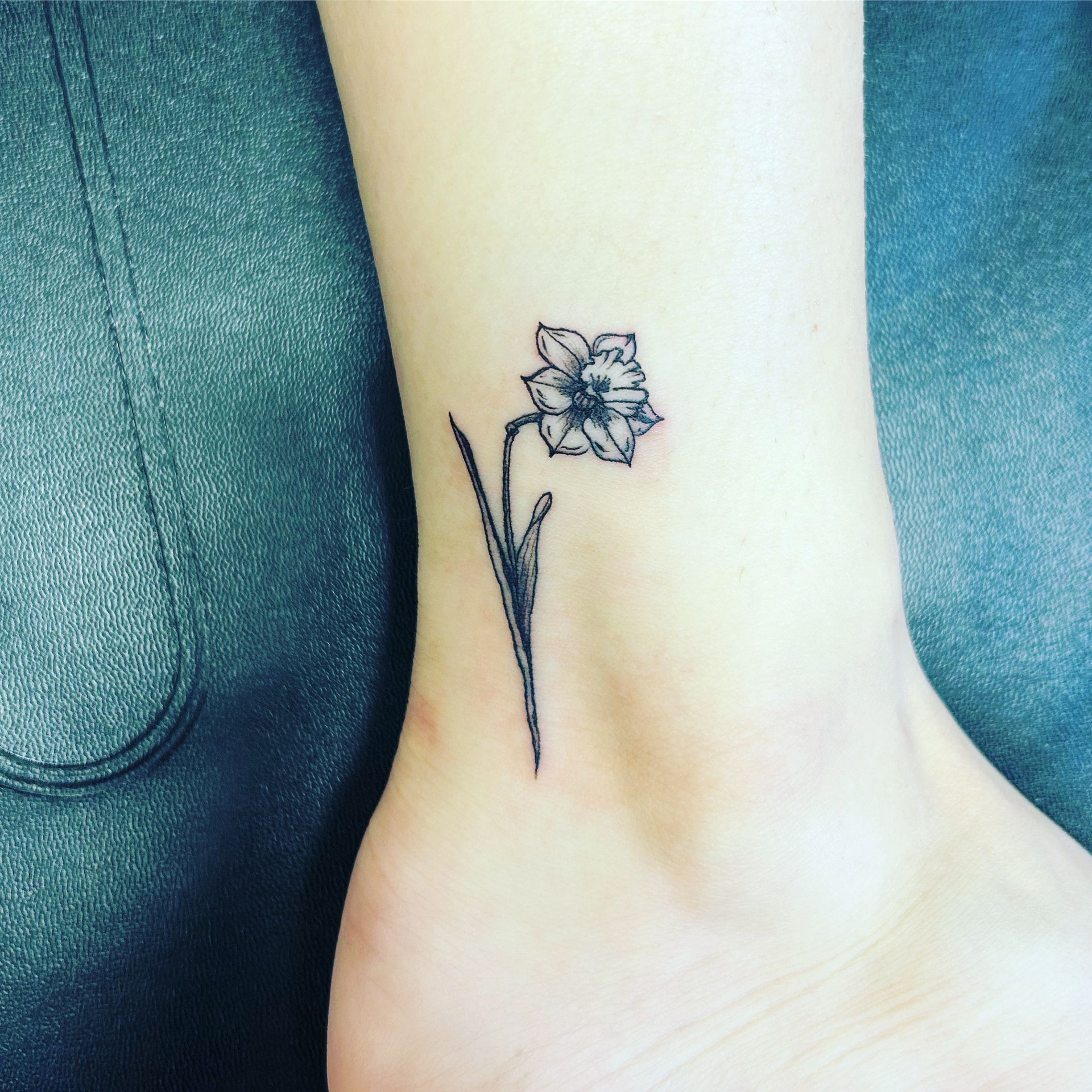 A small black and white flower tattoo on a person 's ankle