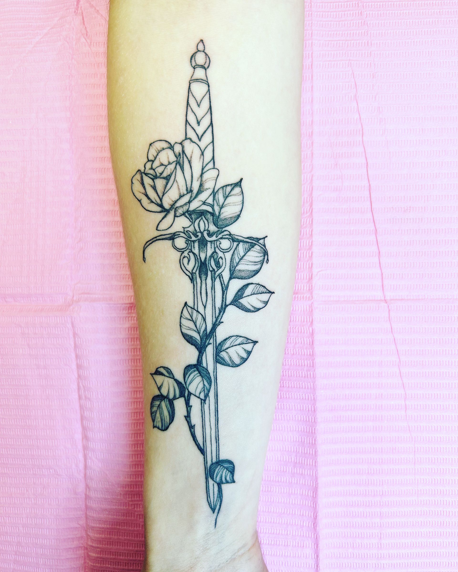 A person has a tattoo of a dagger and roses on their forearm