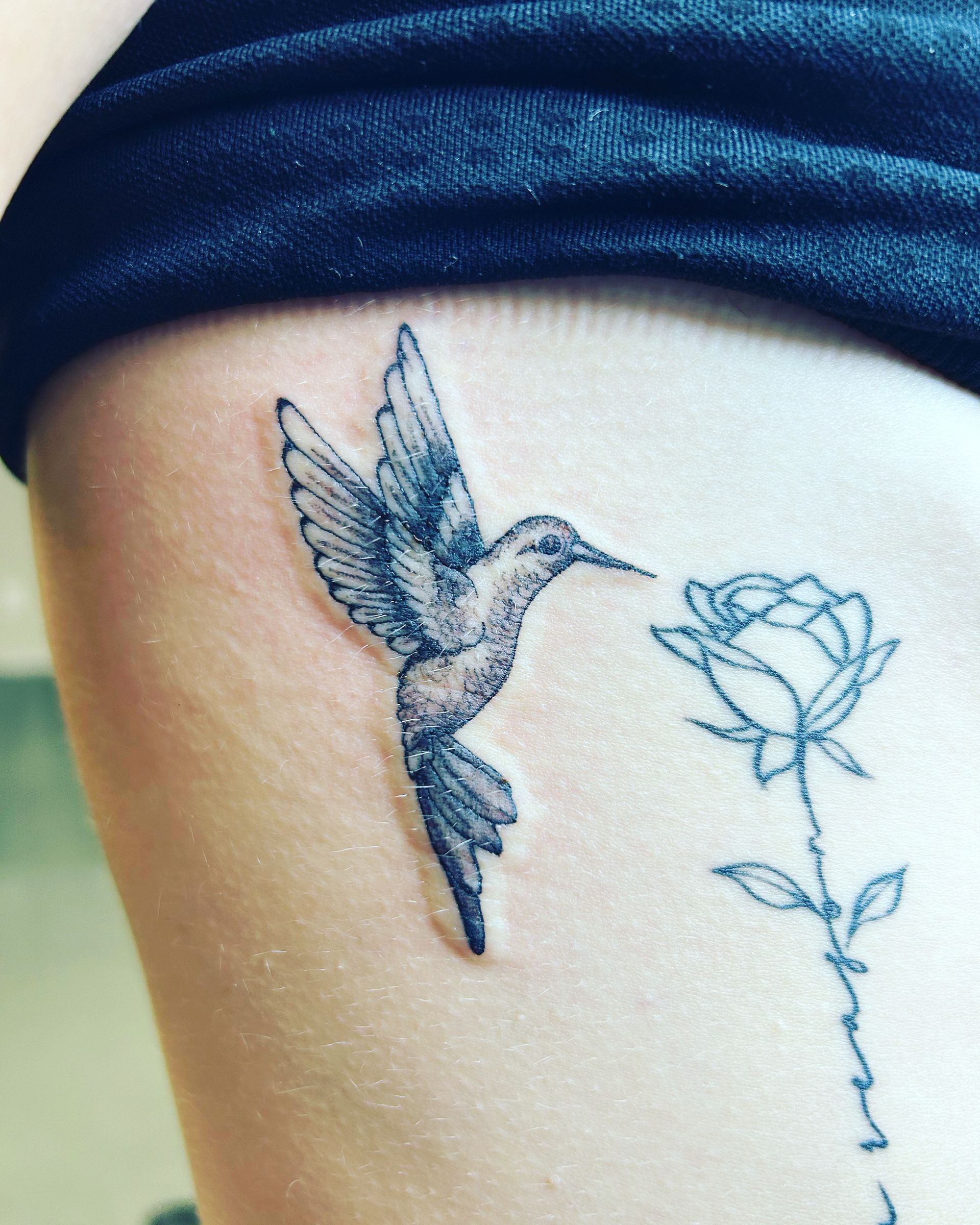 A woman has a tattoo of a hummingbird and a rose