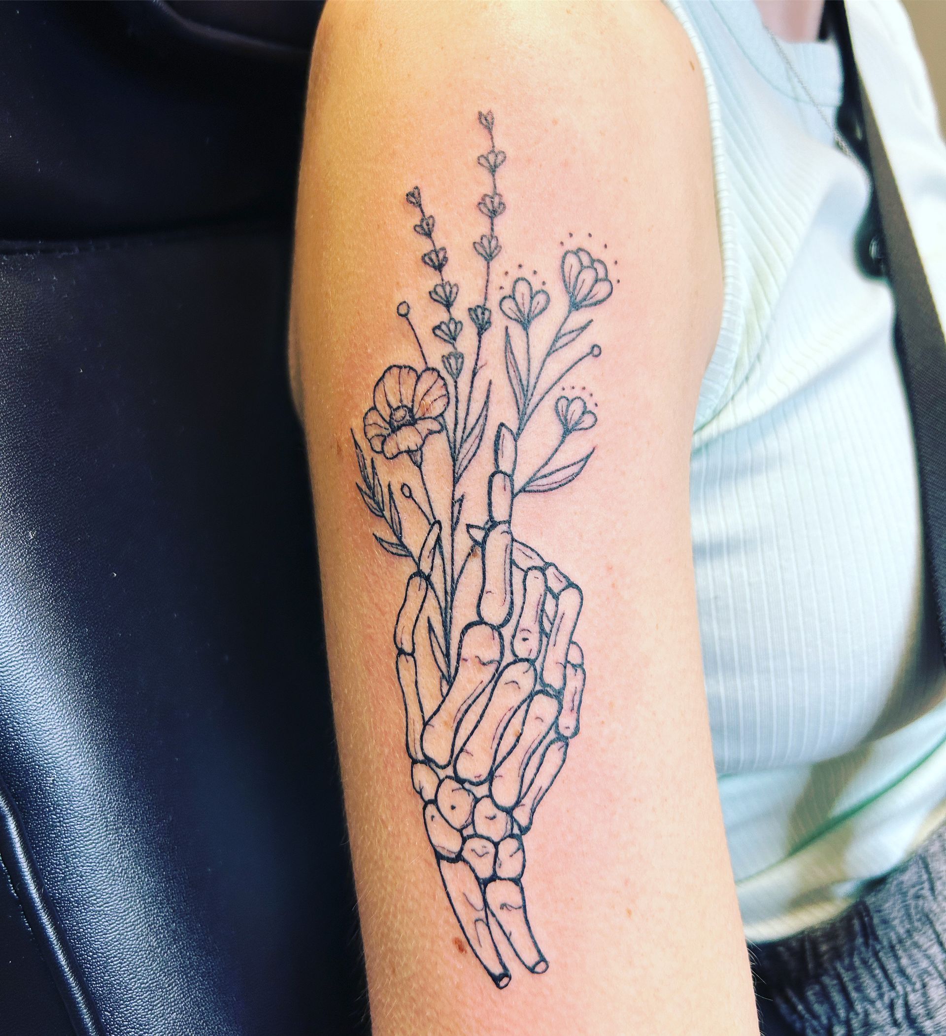 A tattoo of a skeleton hand holding flowers on a woman 's arm