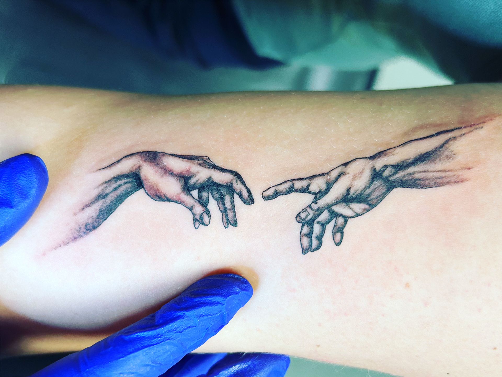 A person has a tattoo of the creation of adam on their arm