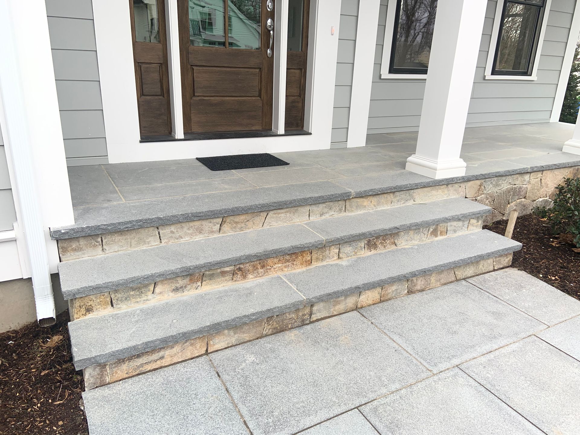 Front porch with gray stone steps, white columns, and a brown front door.