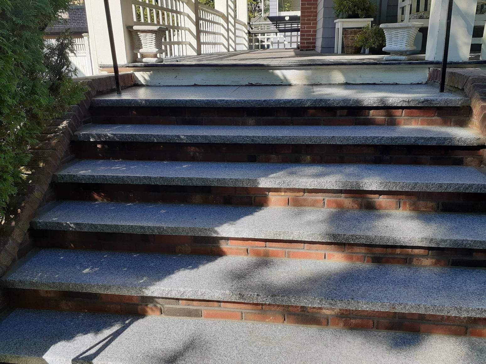 Brick steps with dark railings and sunlight shadows leading up to a house entrance
