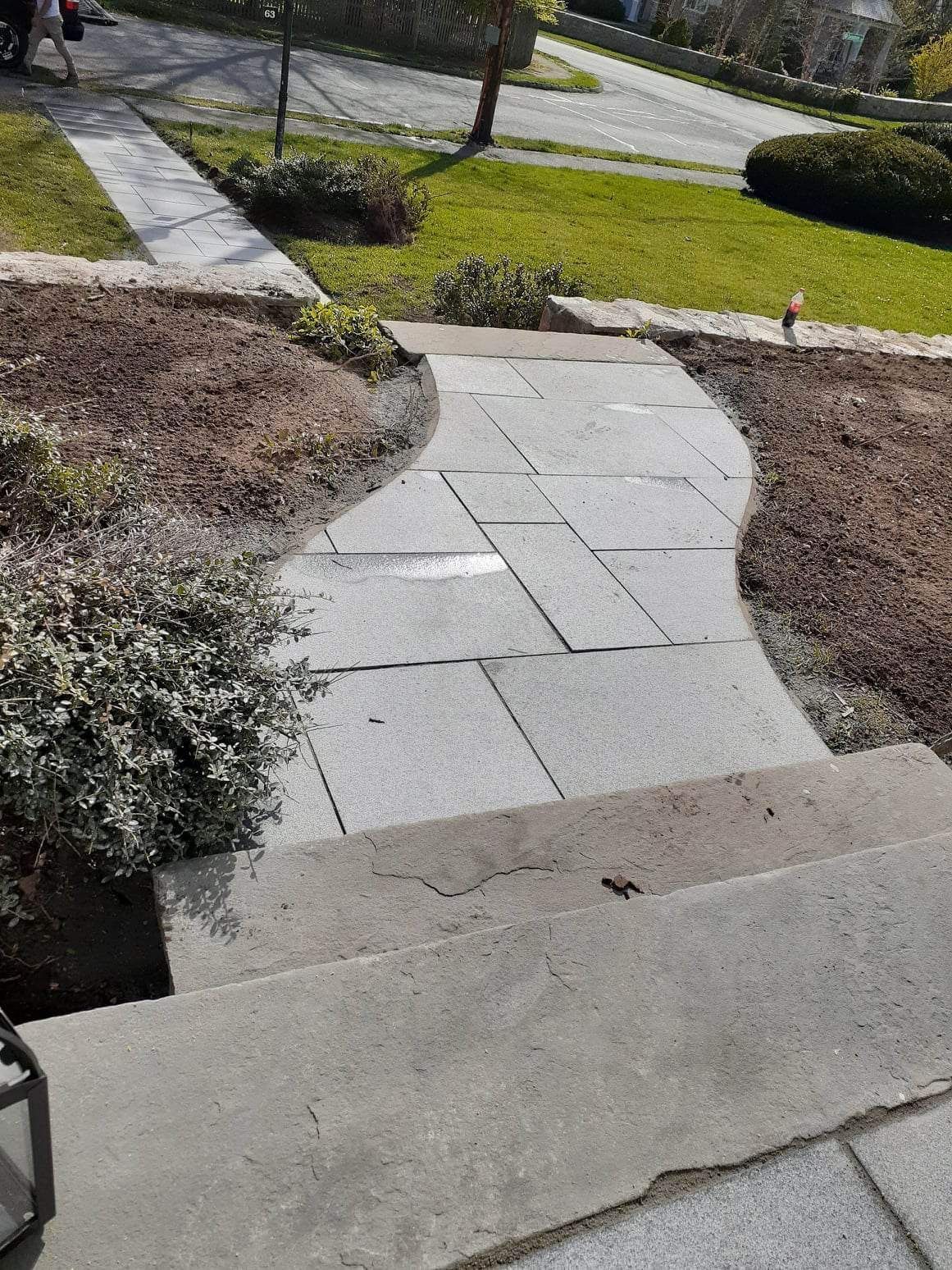 Stone walkway and concrete steps leading through a landscaped yard with grass and shrubs.