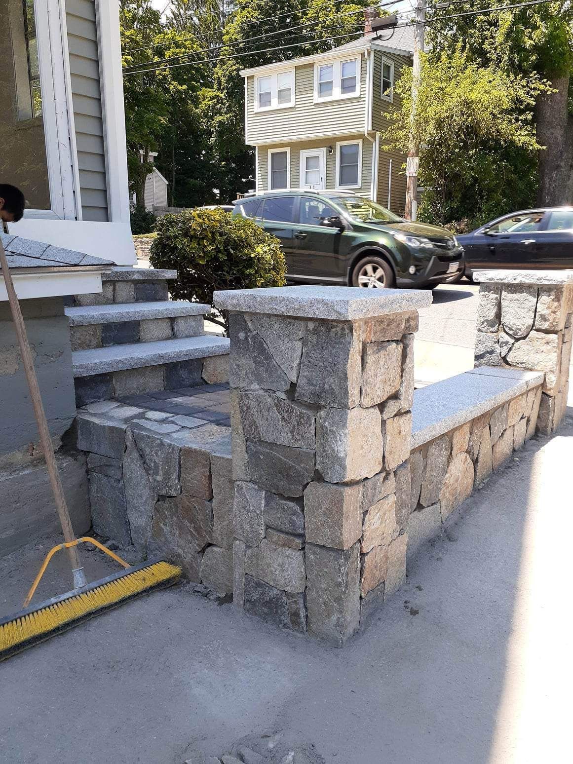 Stone front steps and low retaining wall beside a driveway, with a parked car and house in the background