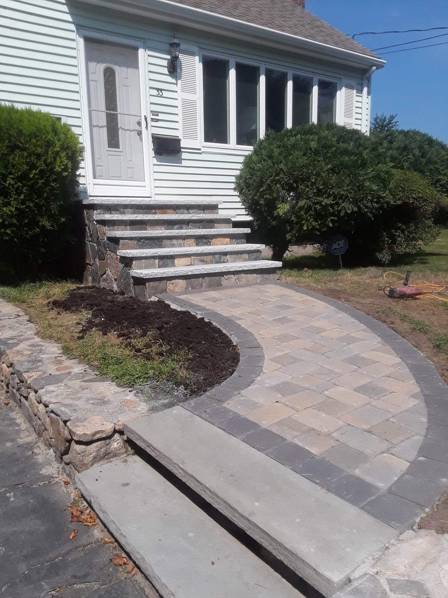 Curved paver walkway leading to a house entrance with steps and shrubs on either side