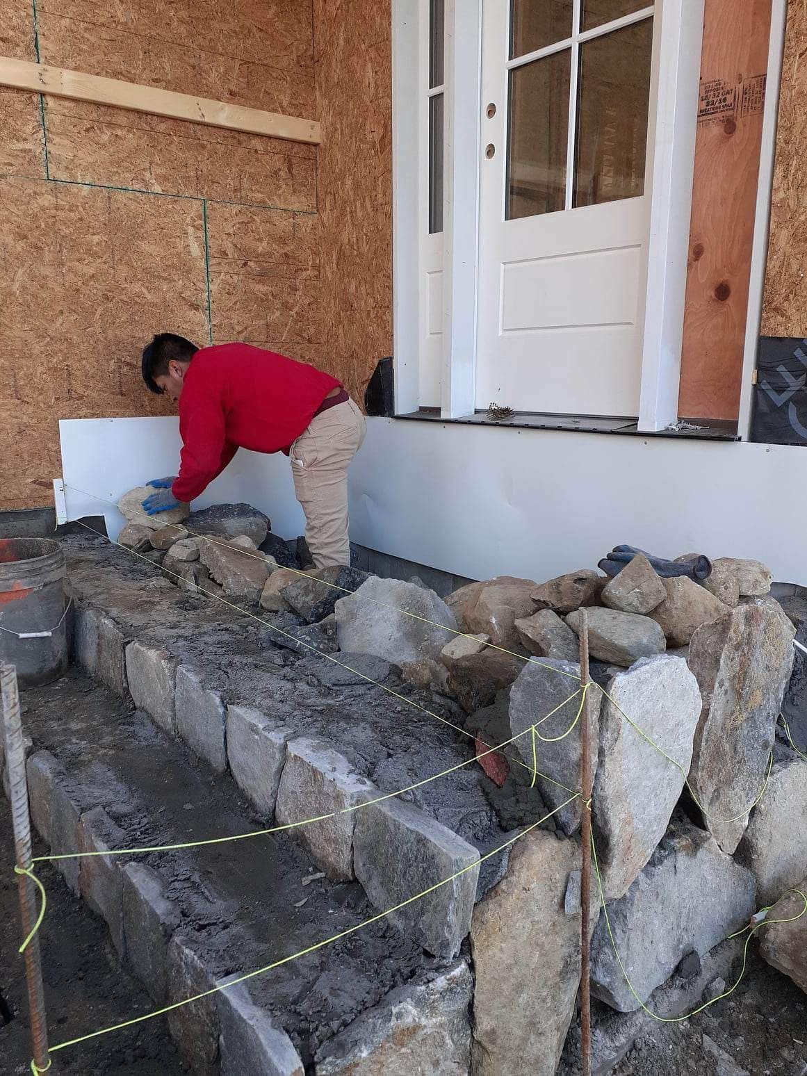 Worker in a red shirt leveling stone steps beside a house entrance