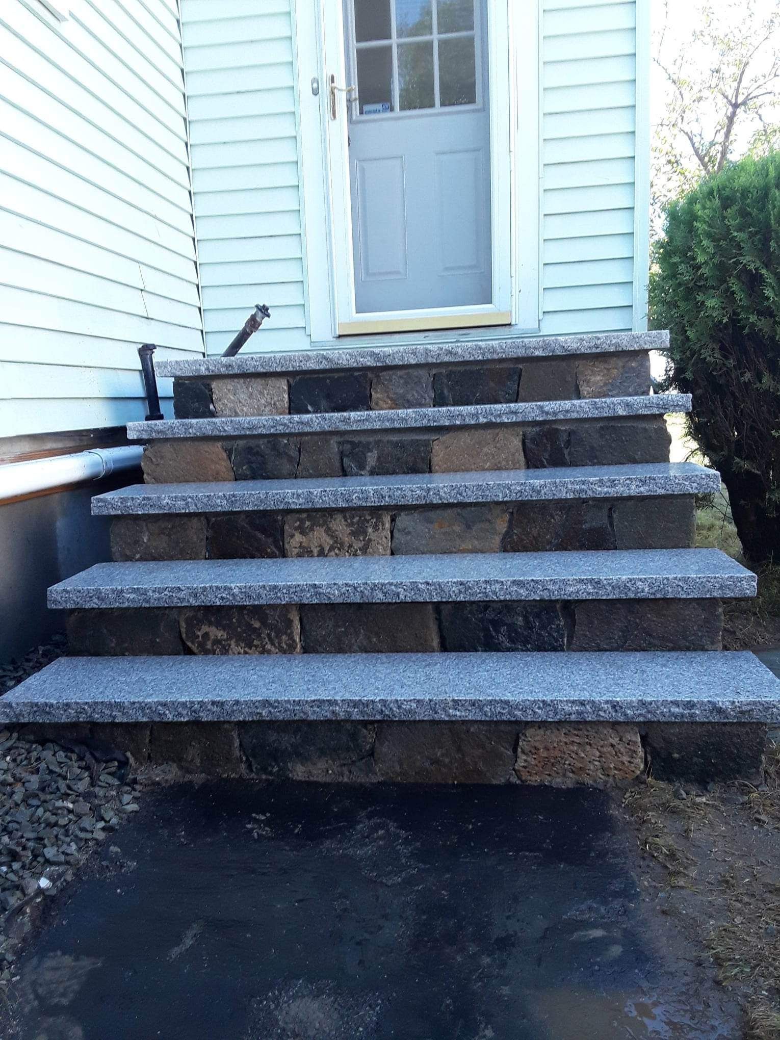 Front steps with dark textured treads leading to a light blue door beside white siding.