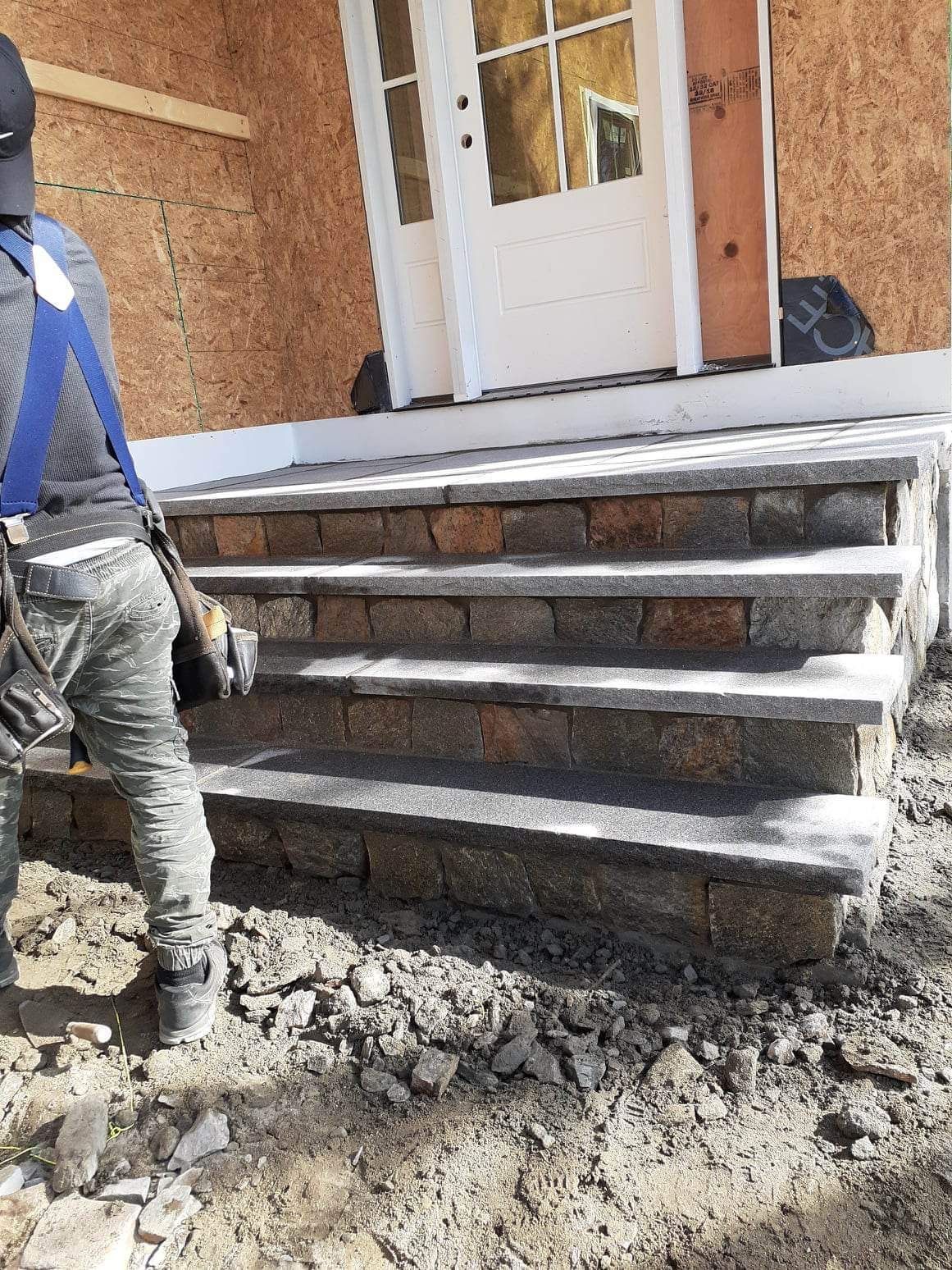Worker installing concrete steps at a house entrance with white door and unfinished porch.