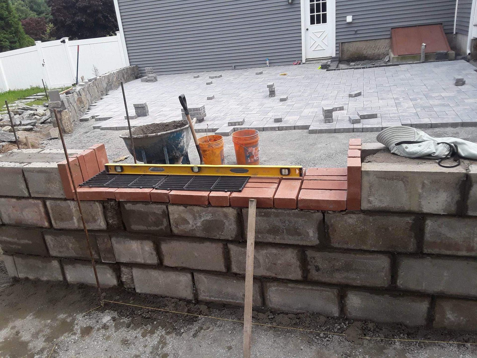 Stone garden wall under construction with a level tool and bricks on top, in a gravel backyard