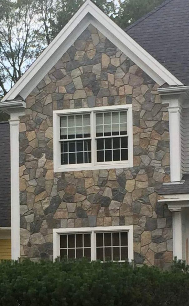 Stone-front house facade with two white-trimmed windows and gray roofline