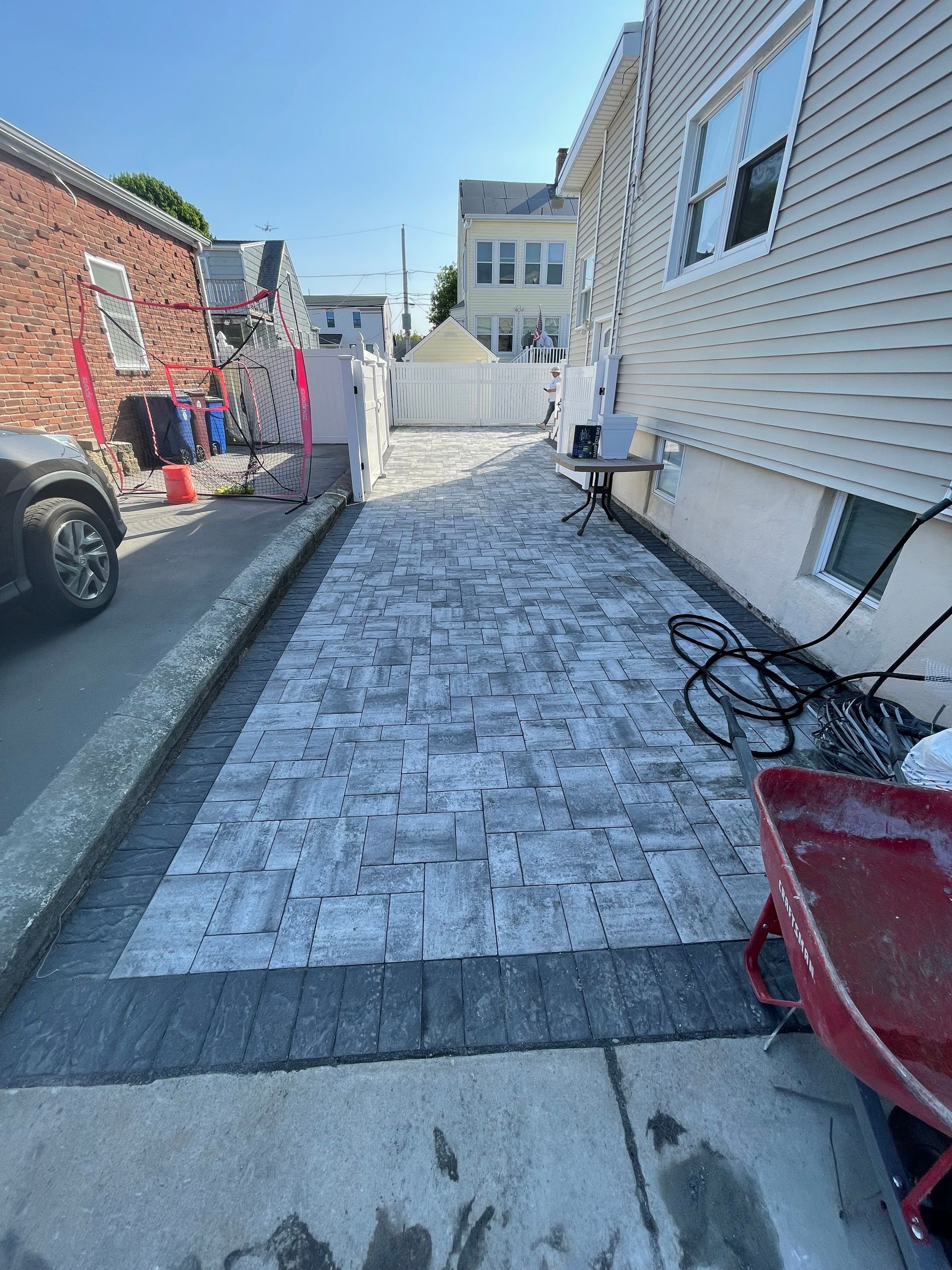 Narrow alley with brick and white siding buildings, snow-covered ground, and a wheelbarrow on the right