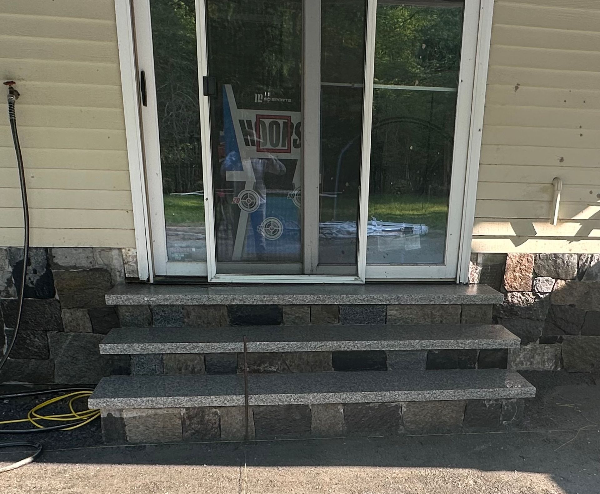 Front steps and glass door entrance to a beige house with stone risers and black handrail holders