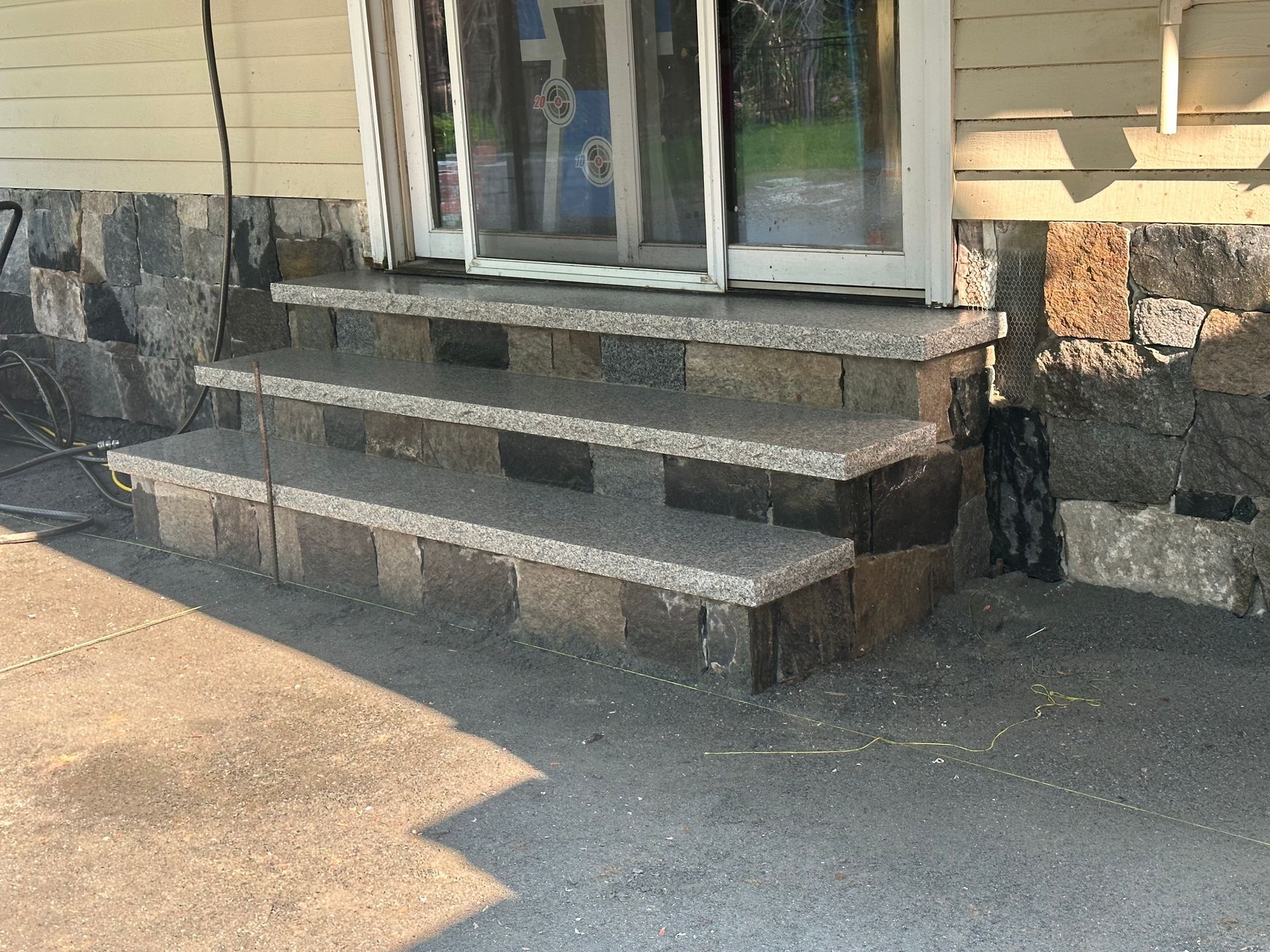 Concrete front steps leading to a house entrance with a glass door and stone siding