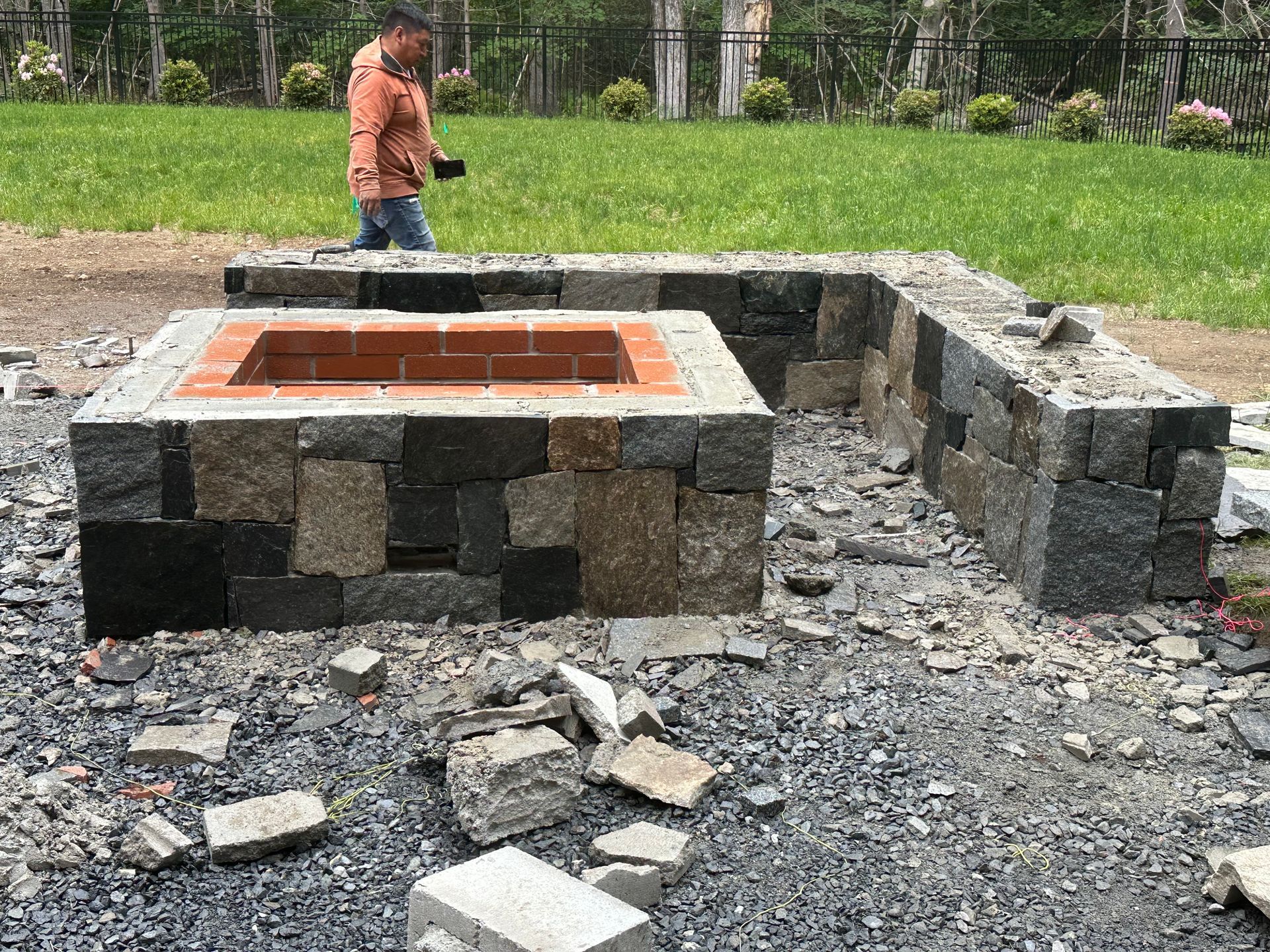 Stone fire pit under construction in a gravel area, with a person standing nearby