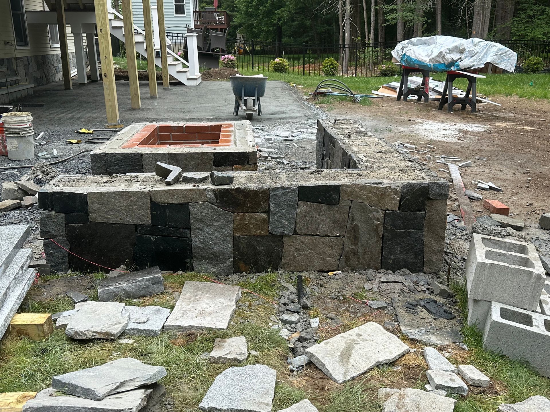 Partially built stone fire pit and retaining wall in a yard, with cinder blocks and construction debris nearby