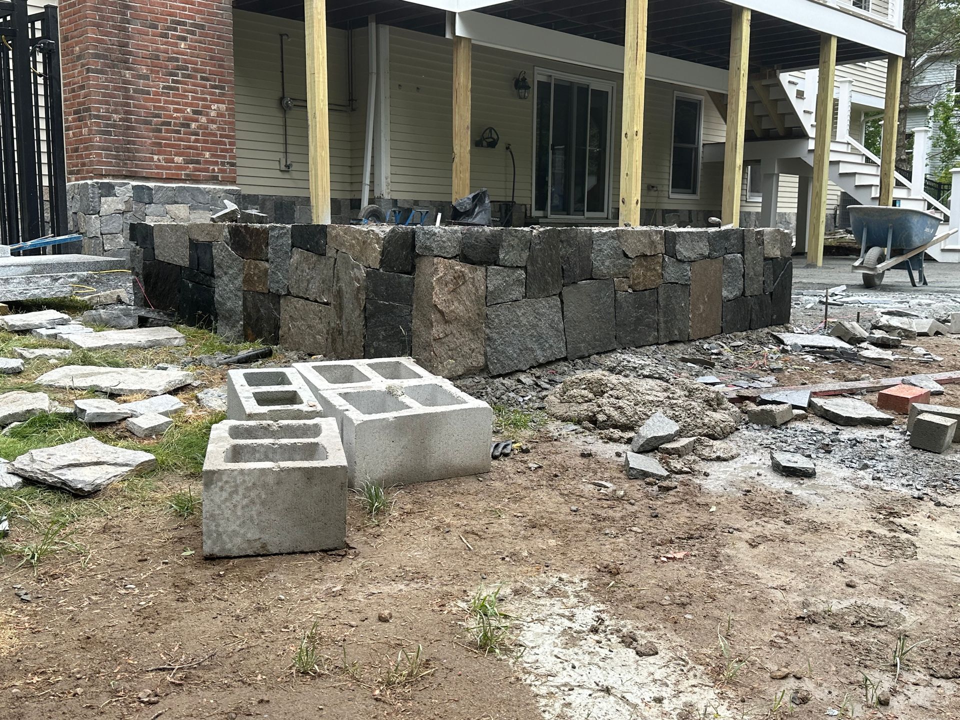 Partially built stone retaining wall and cinder blocks beside a house under construction