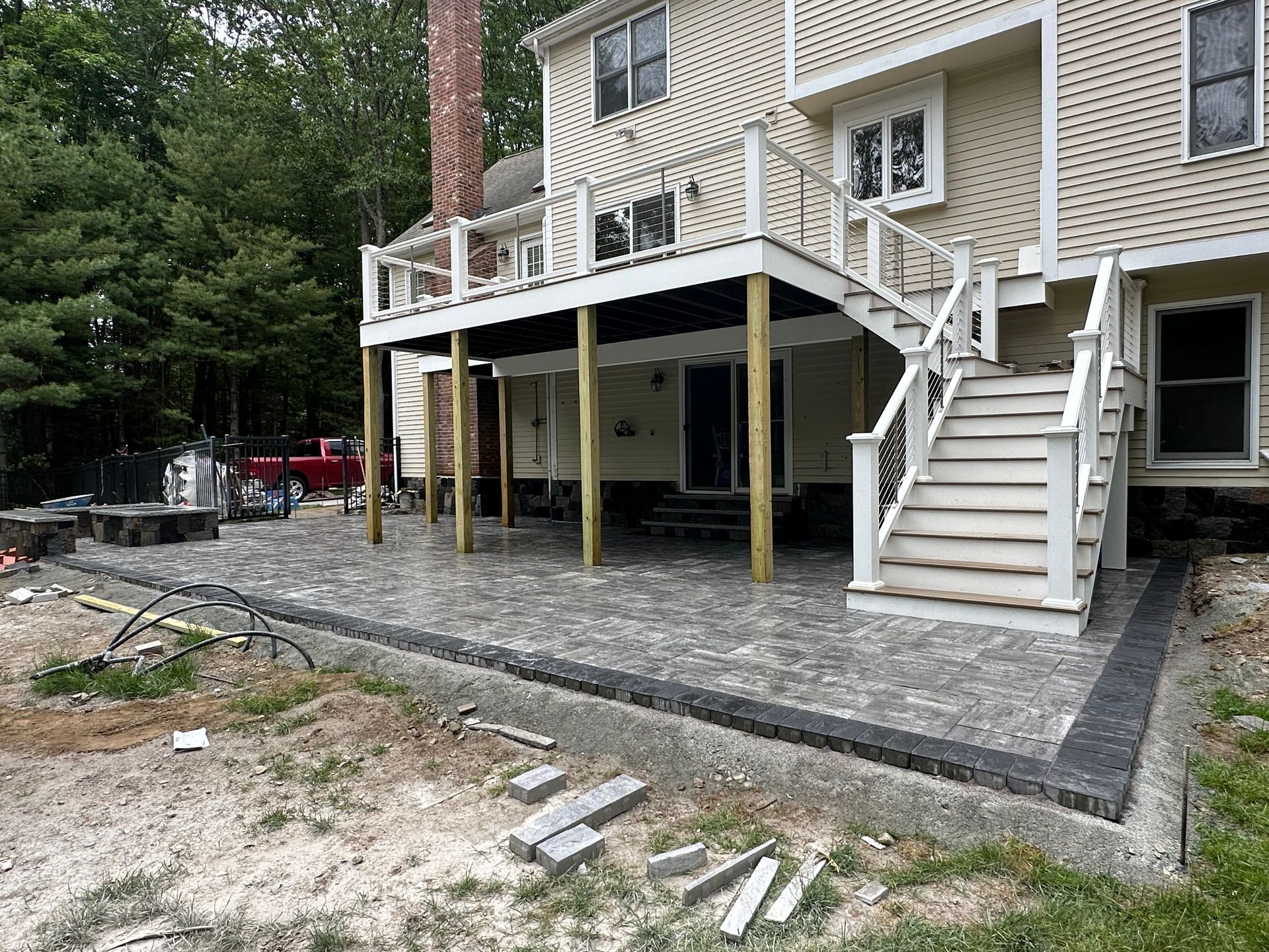 Raised wooden deck under construction beside a beige house, with stairs, support posts, and gravel base.