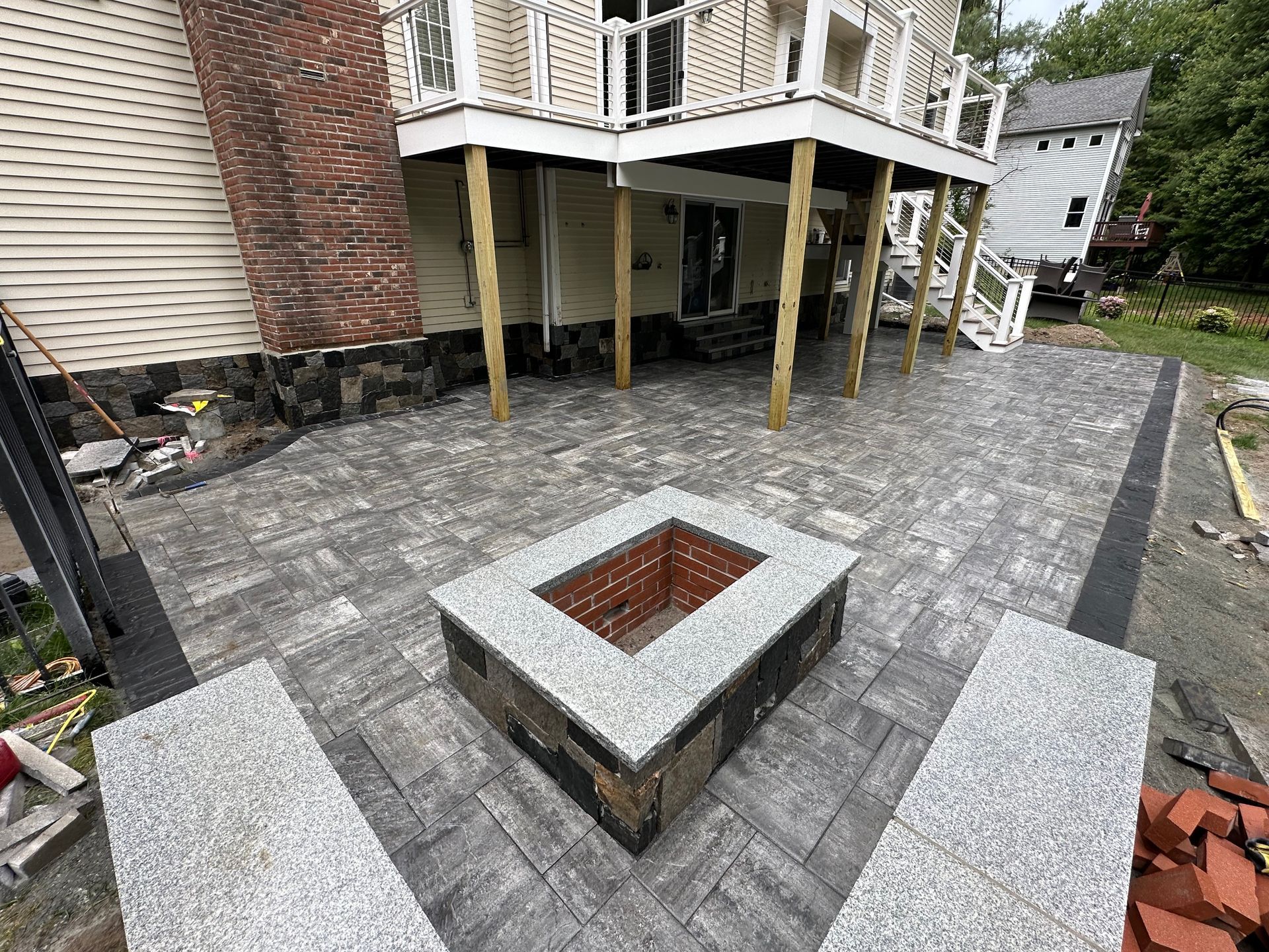 Backyard patio with stone pavers, central fire pit, and house deck in the background
