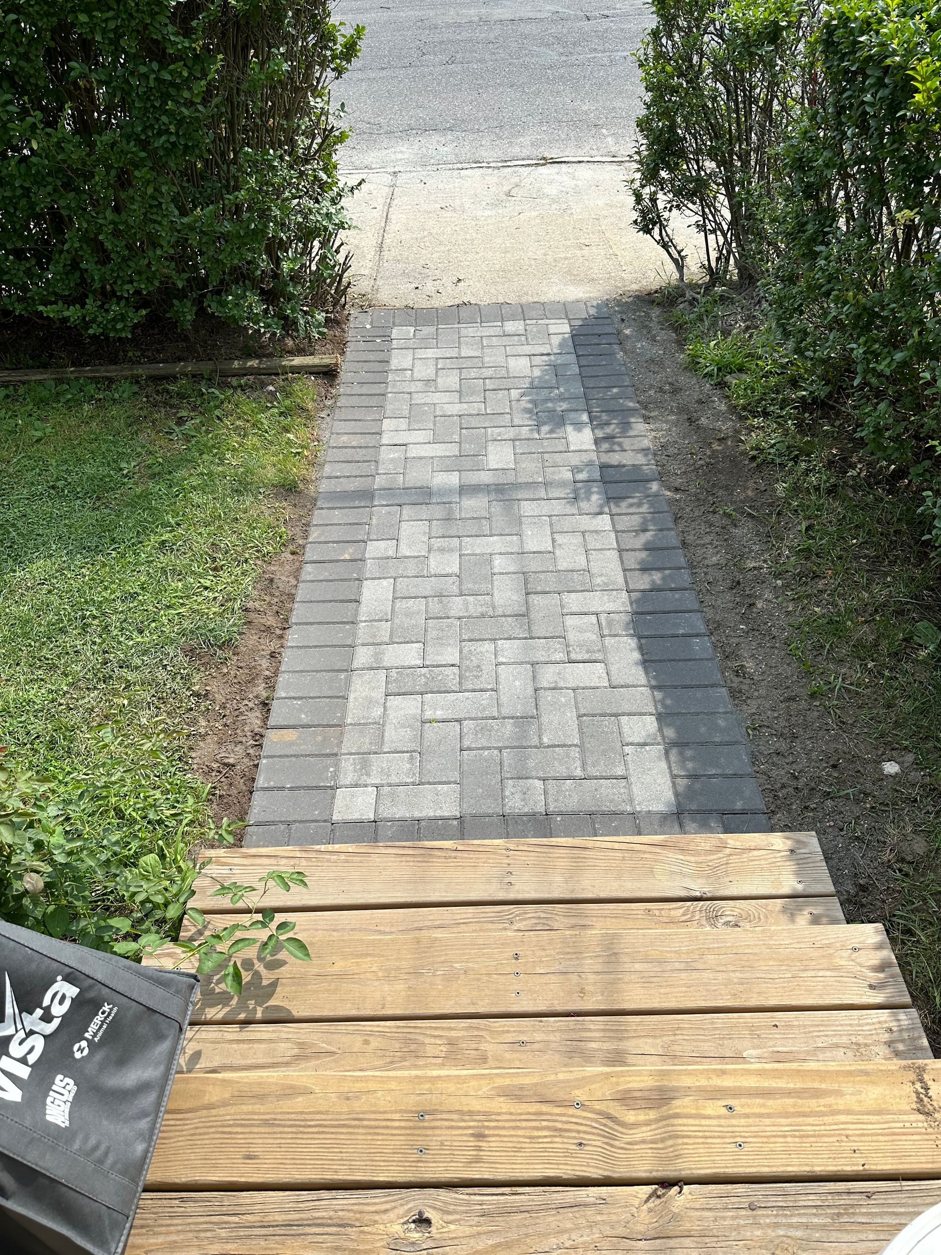 Wooden steps leading to a gray brick path bordered by grass and hedges