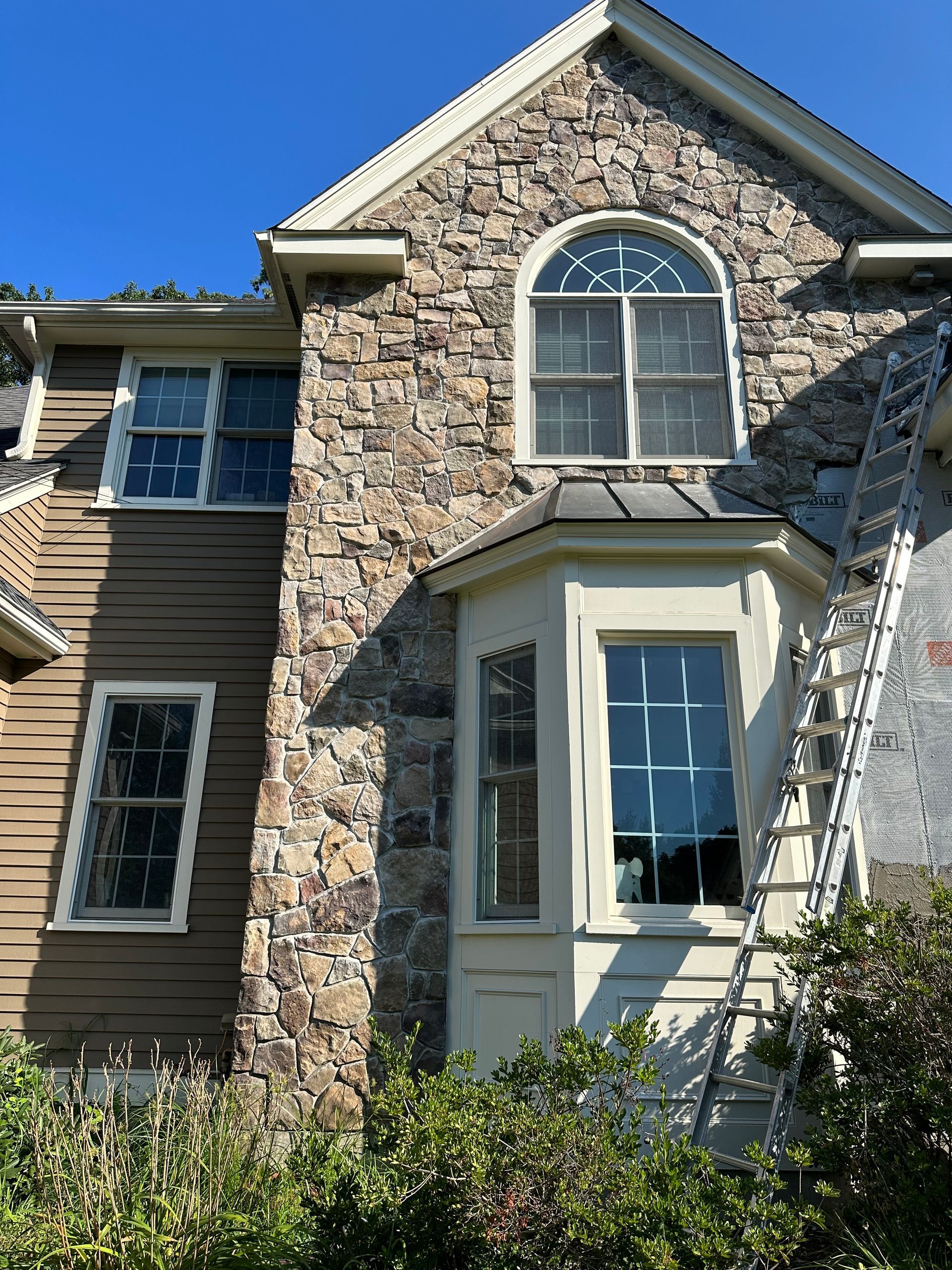 Stone house exterior with arched window, beige siding, and a ladder leaning against the wall