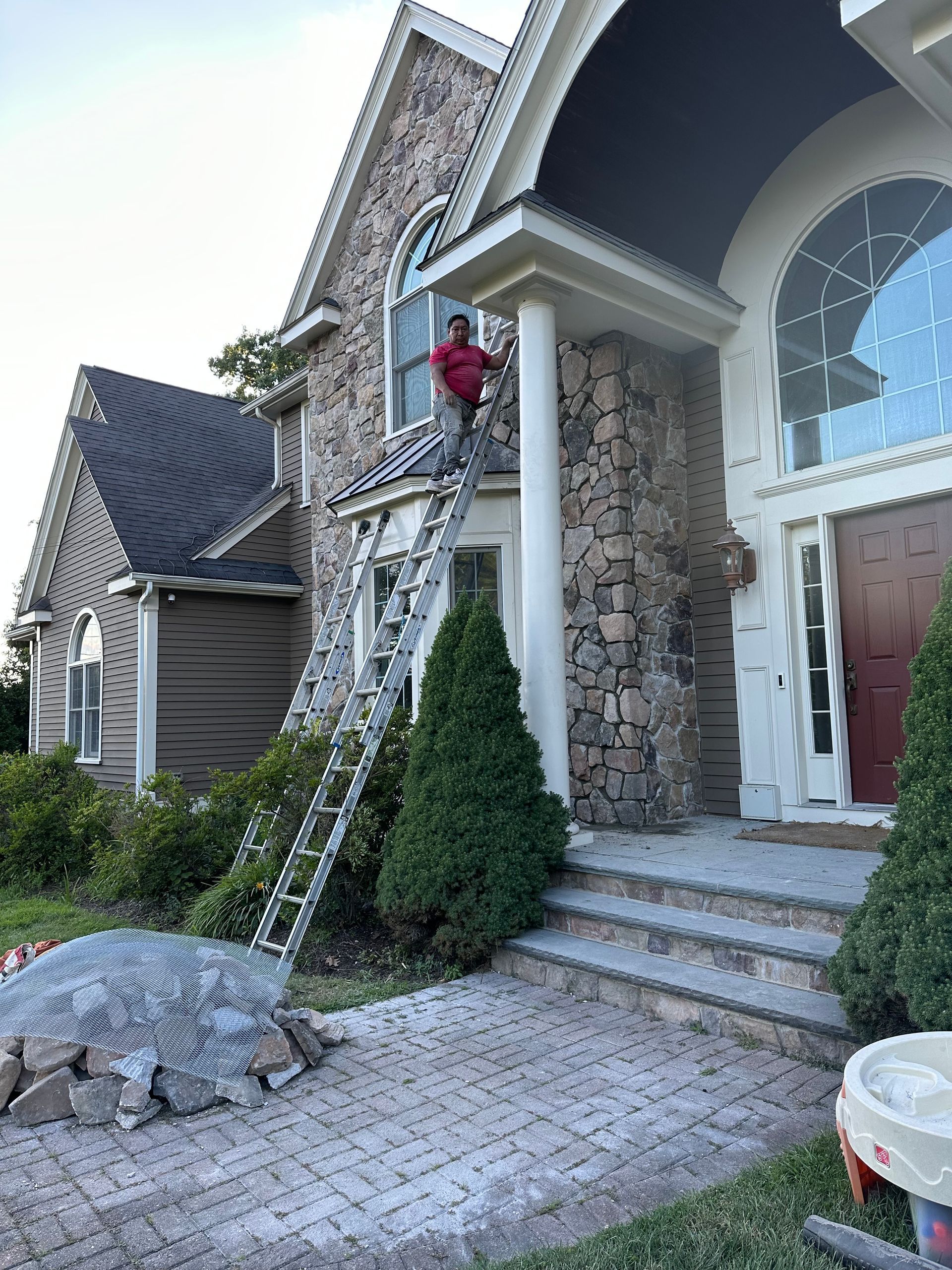 Front entrance of a stone house with red door, arched window, steps, and holiday lights on ladders
