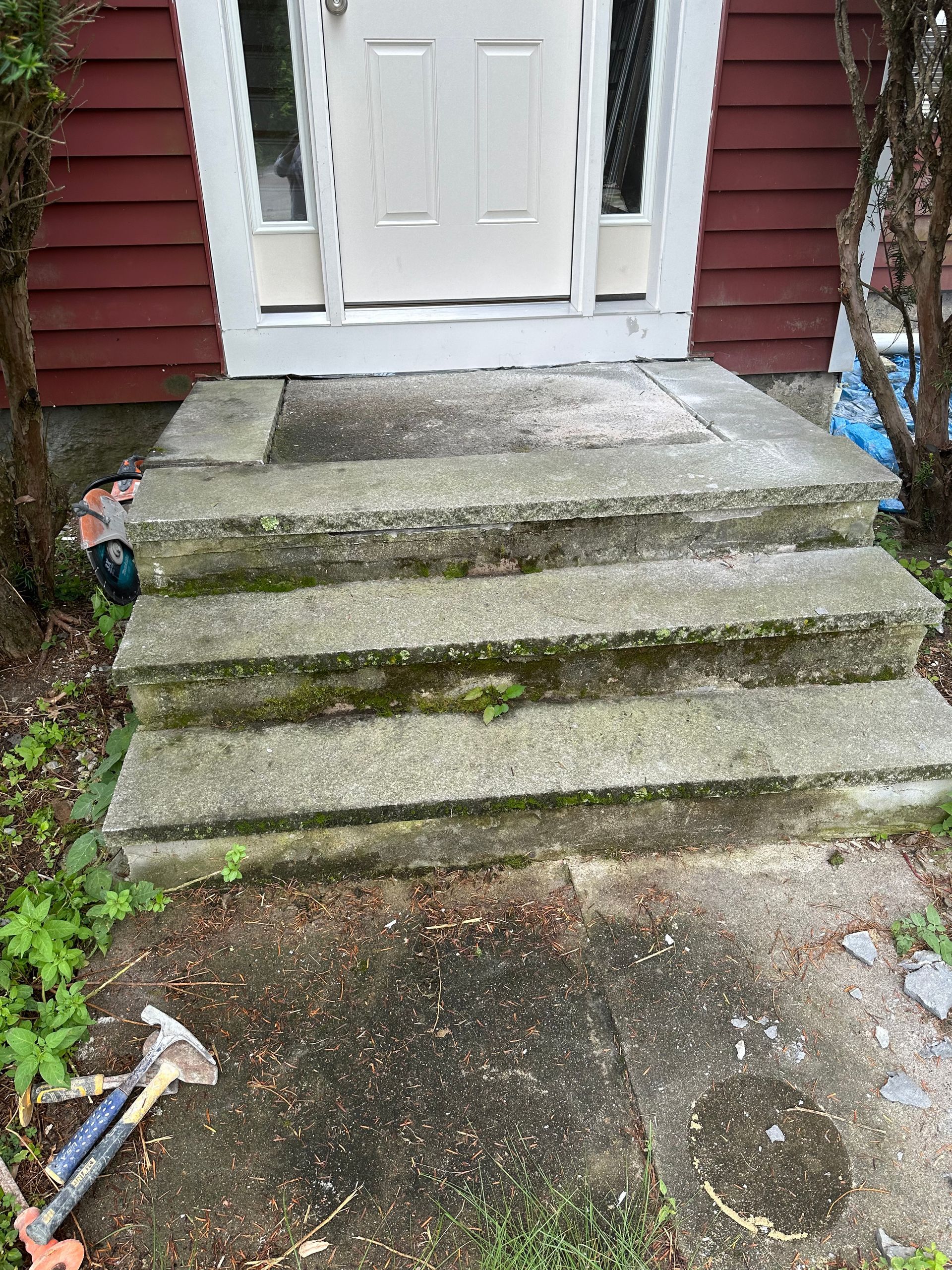 Mossy concrete steps leading to a white door on a red house exterior
