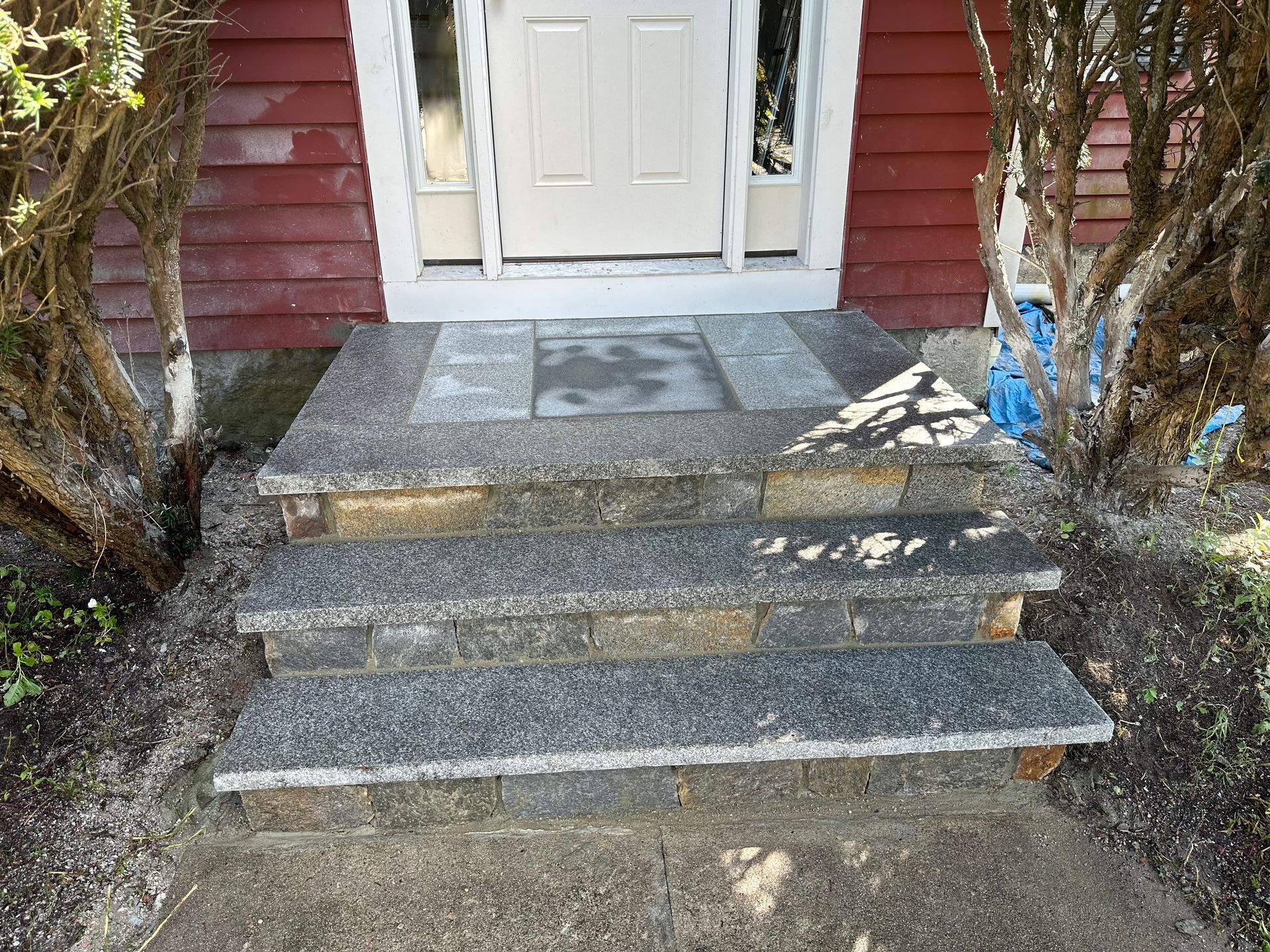 Front steps leading to a white door, with gray stone steps and red siding on either side.