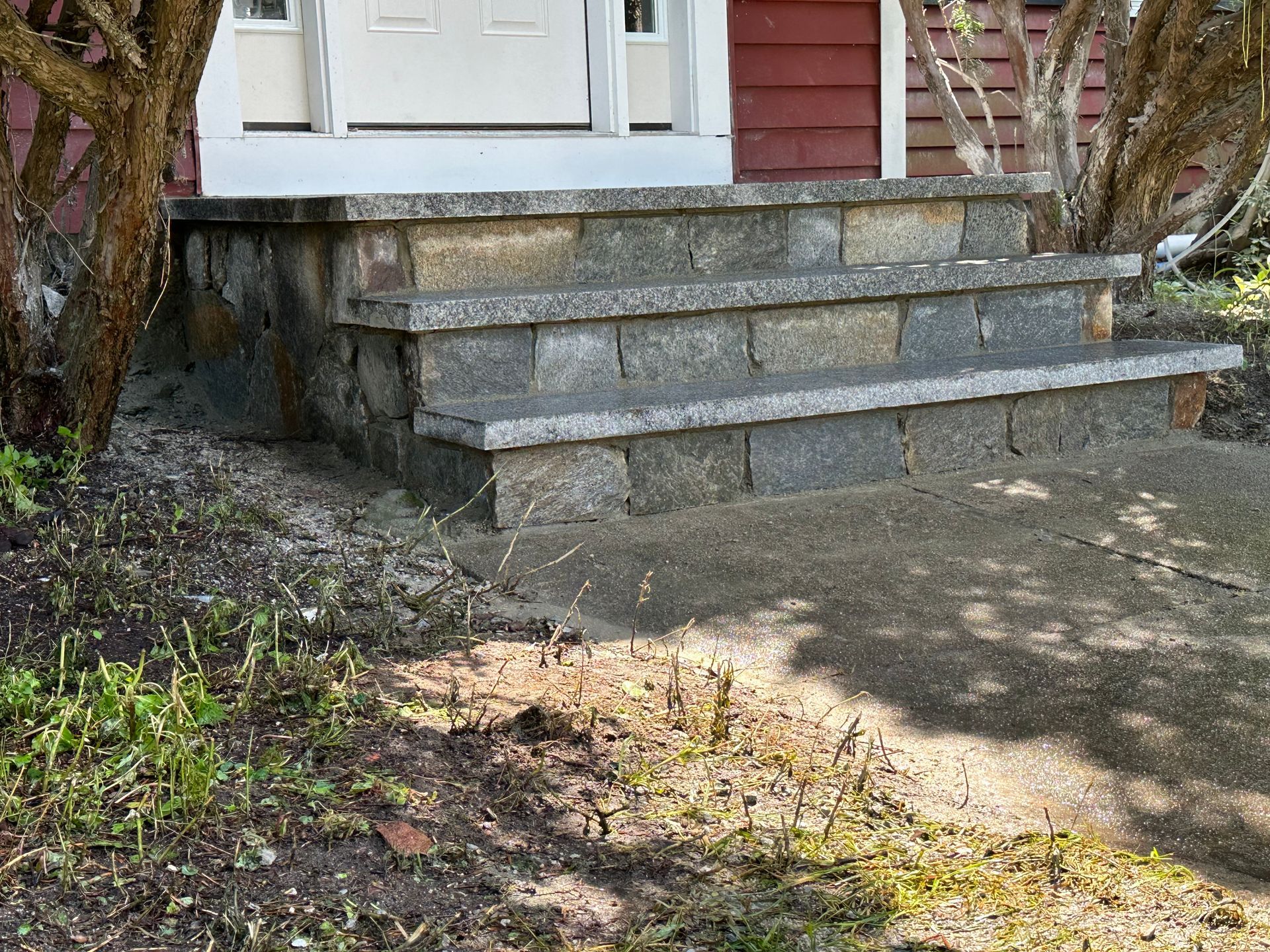 Front steps of a house with stone stairs, a white door, and a brick-and-siding porch area
