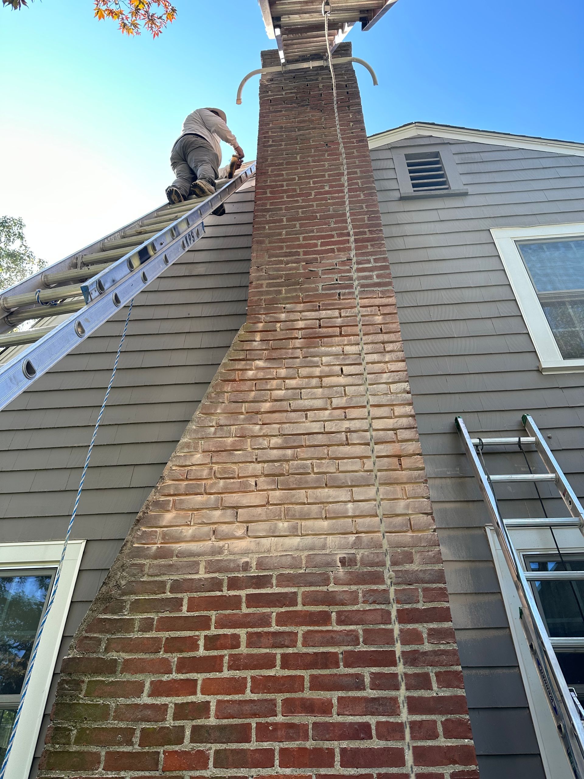 Worker on a ladder inspecting a tall brick chimney on the side of a house