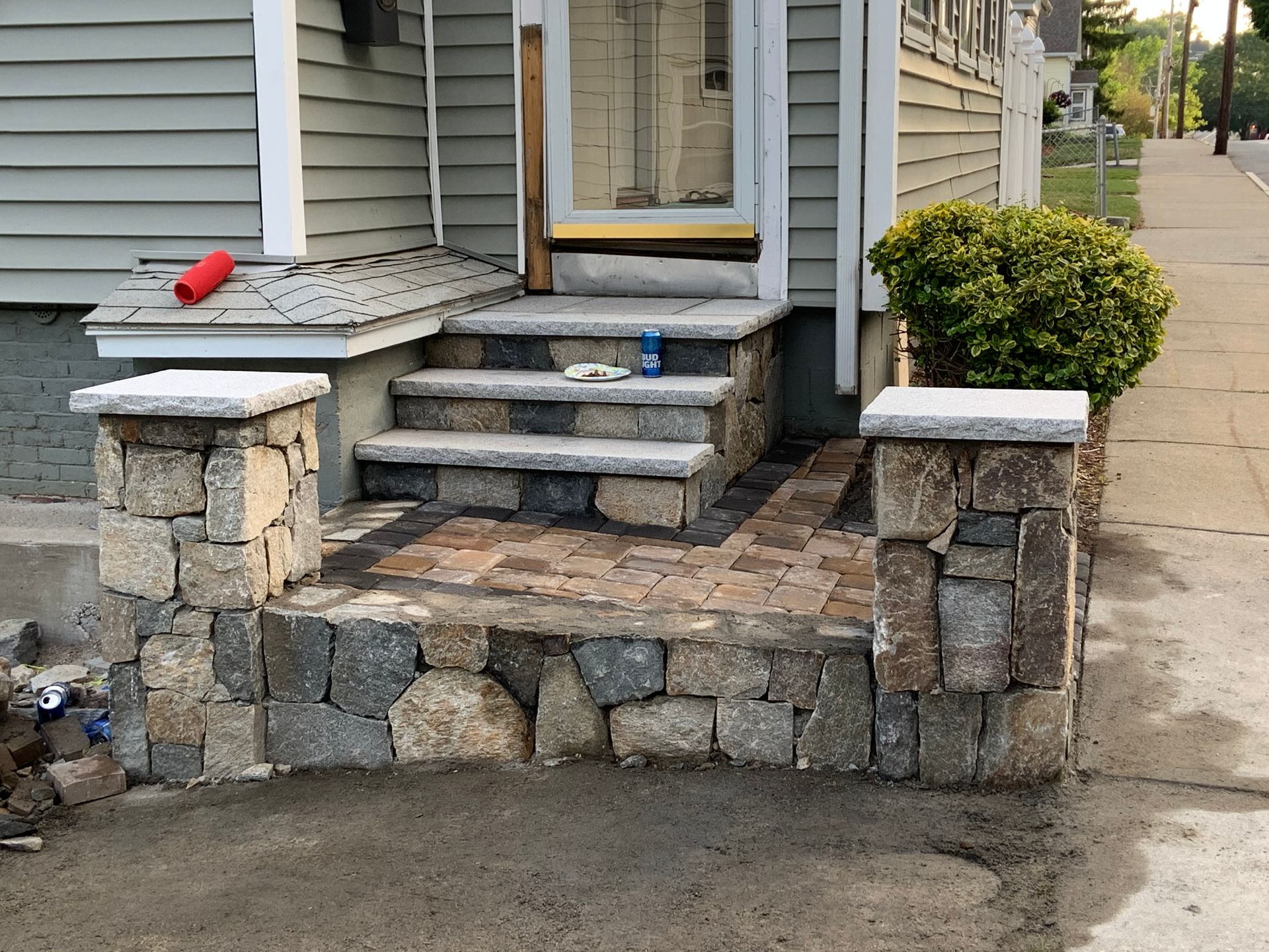 Front steps of a house with stone retaining wall and sidewalk; a red object rests on the left pillar.