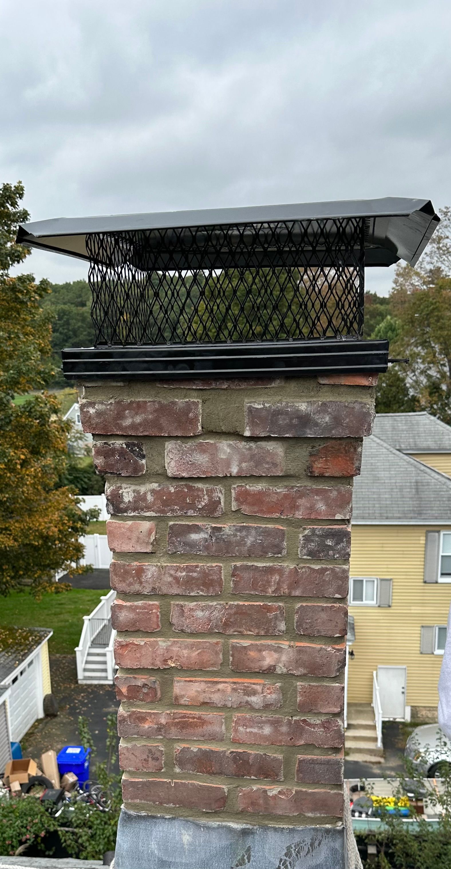 Brick chimney topped with a black metal chimney cap against a cloudy sky.