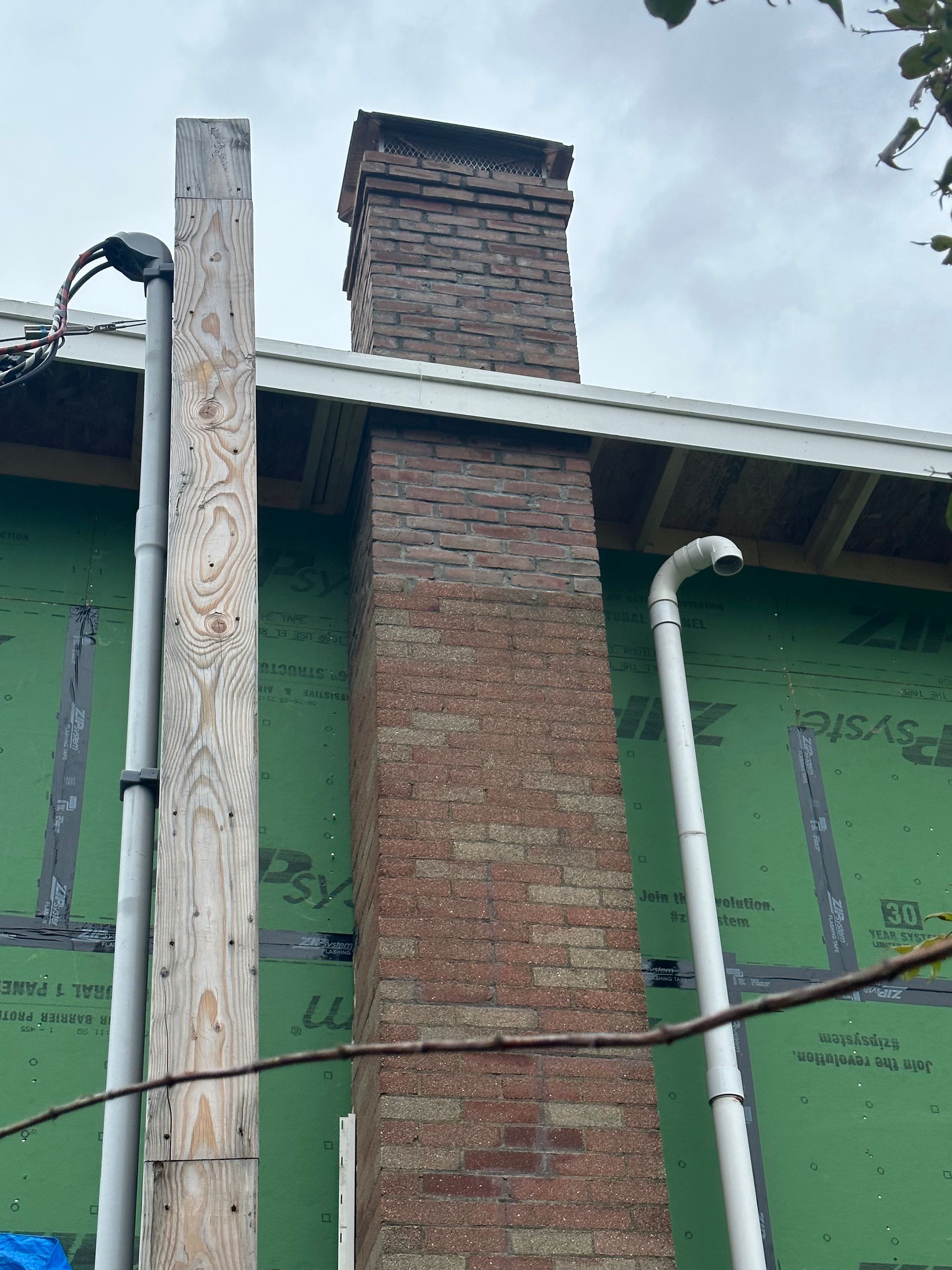 Brick chimney on a green building with a white roof and hanging wires against the sky