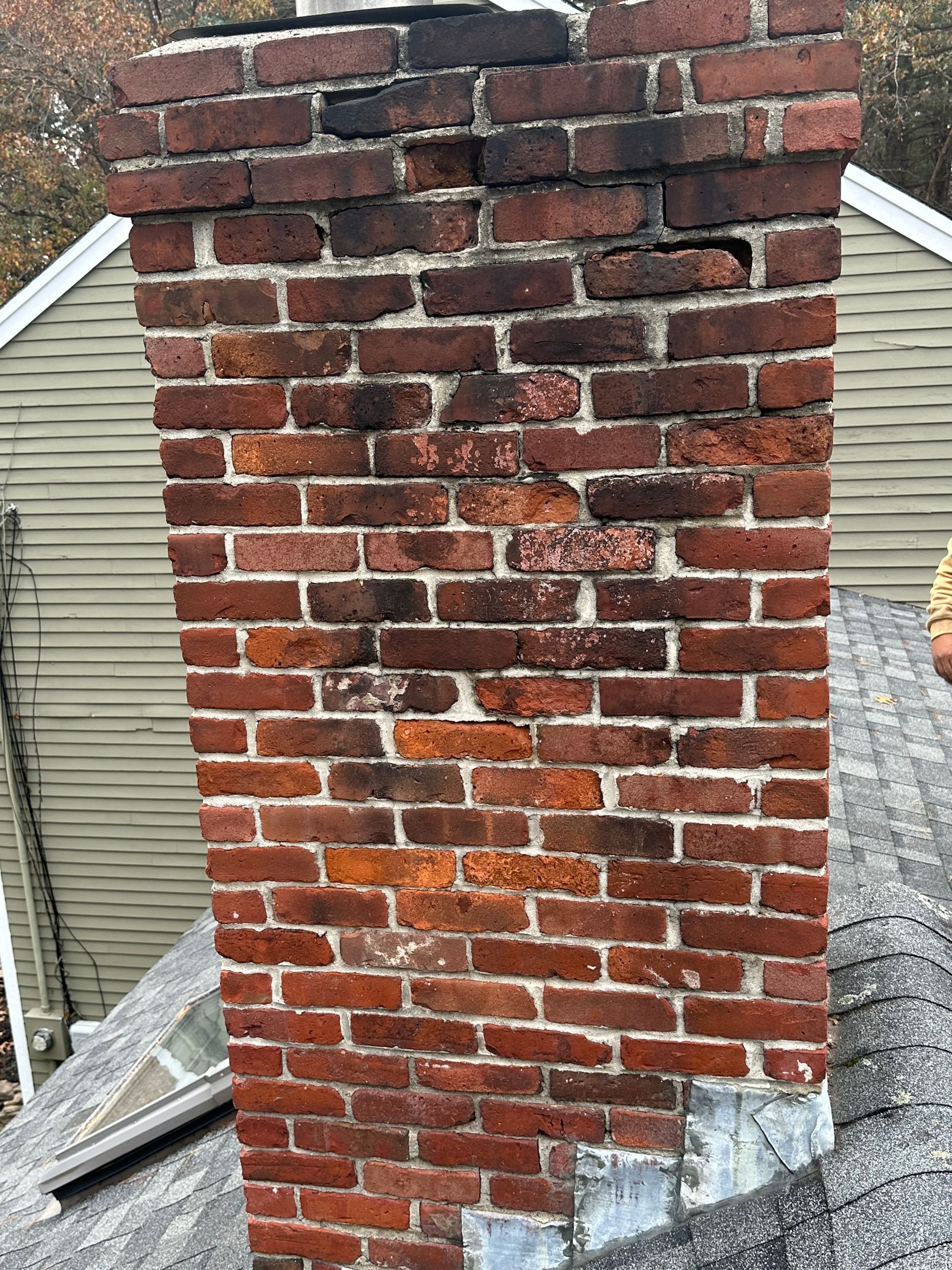 Weathered red-brick chimney with missing mortar and a gray metal flashing at the roofline