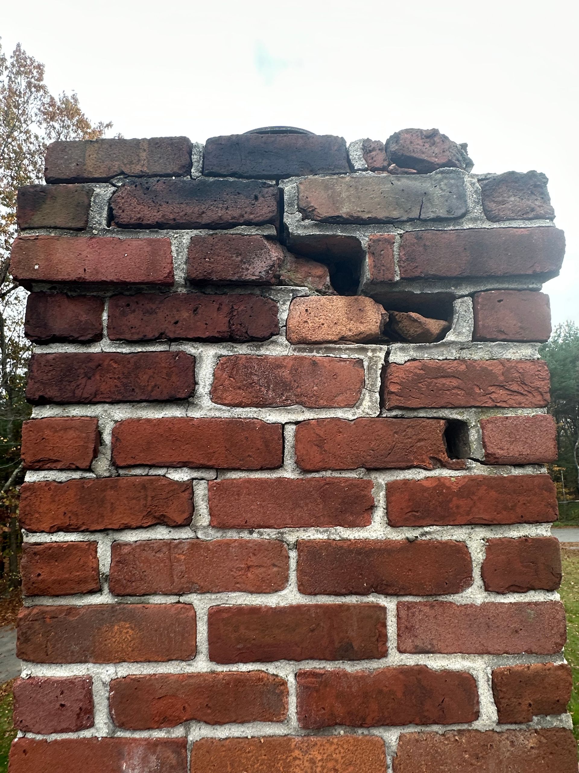 Red brick wall with a damaged, crumbling top and dark soot marks near the upper right