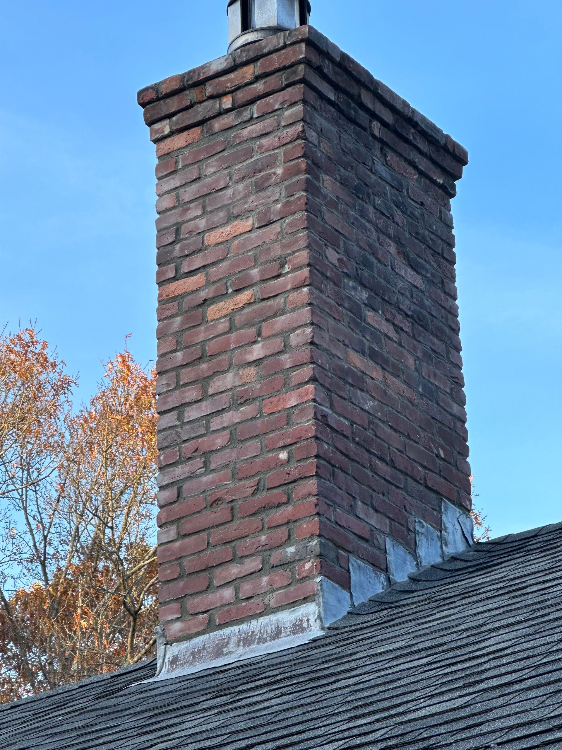 Brick chimney on a shingled roof against a blue sky.