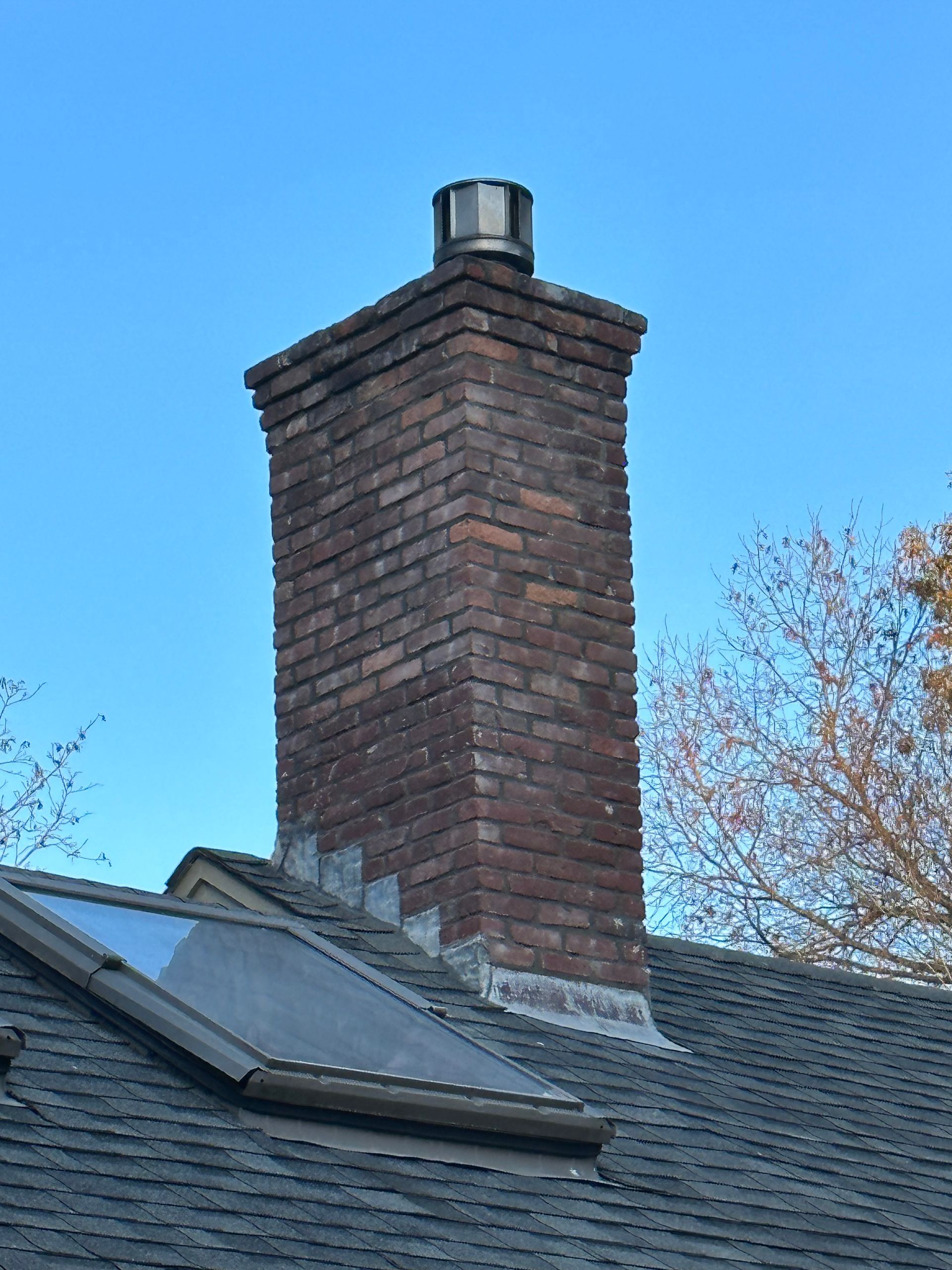 Brick chimney on a shingled roof against a blue sky