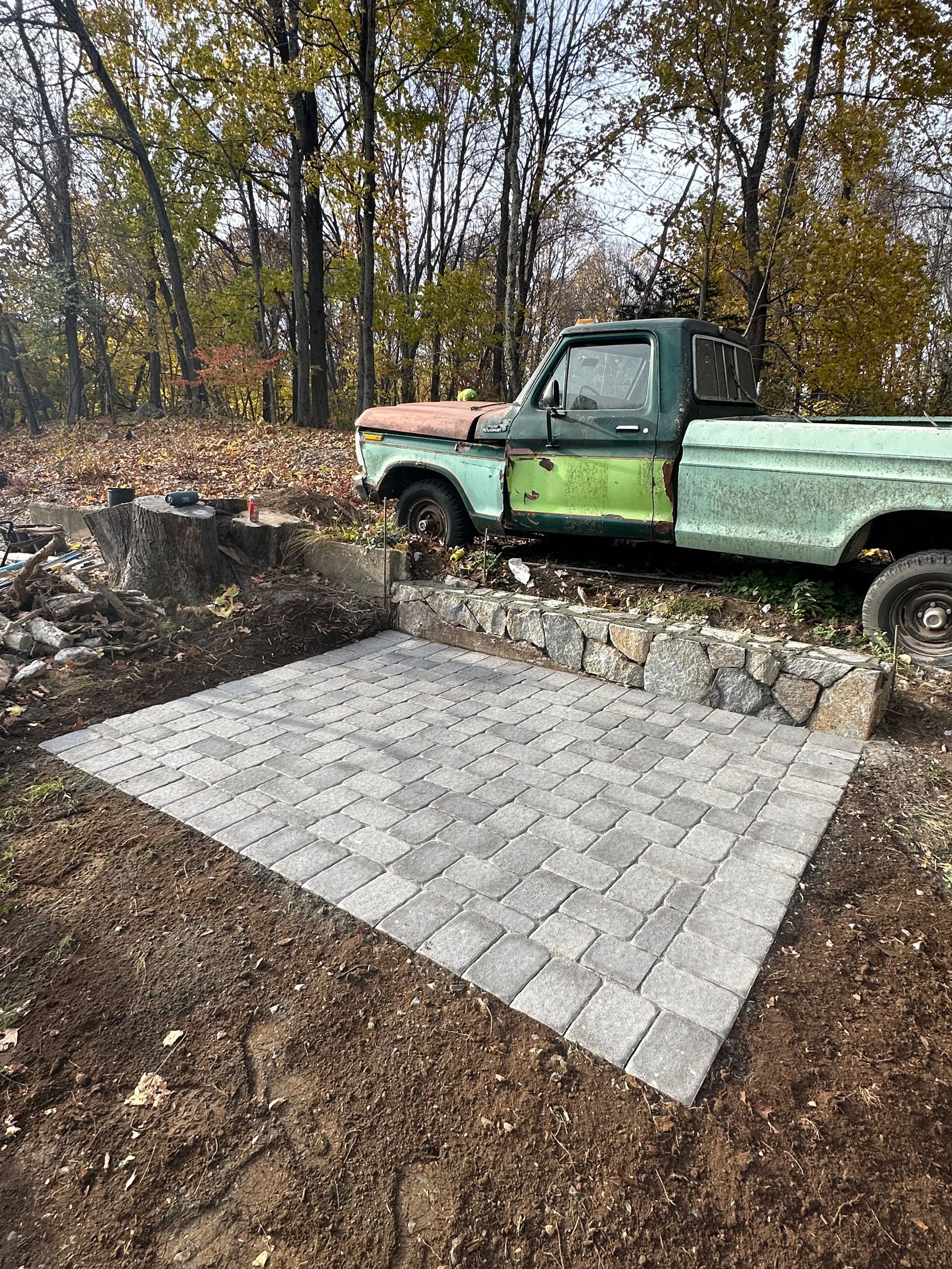 Paved brick patio beside an old green pickup truck in a wooded yard