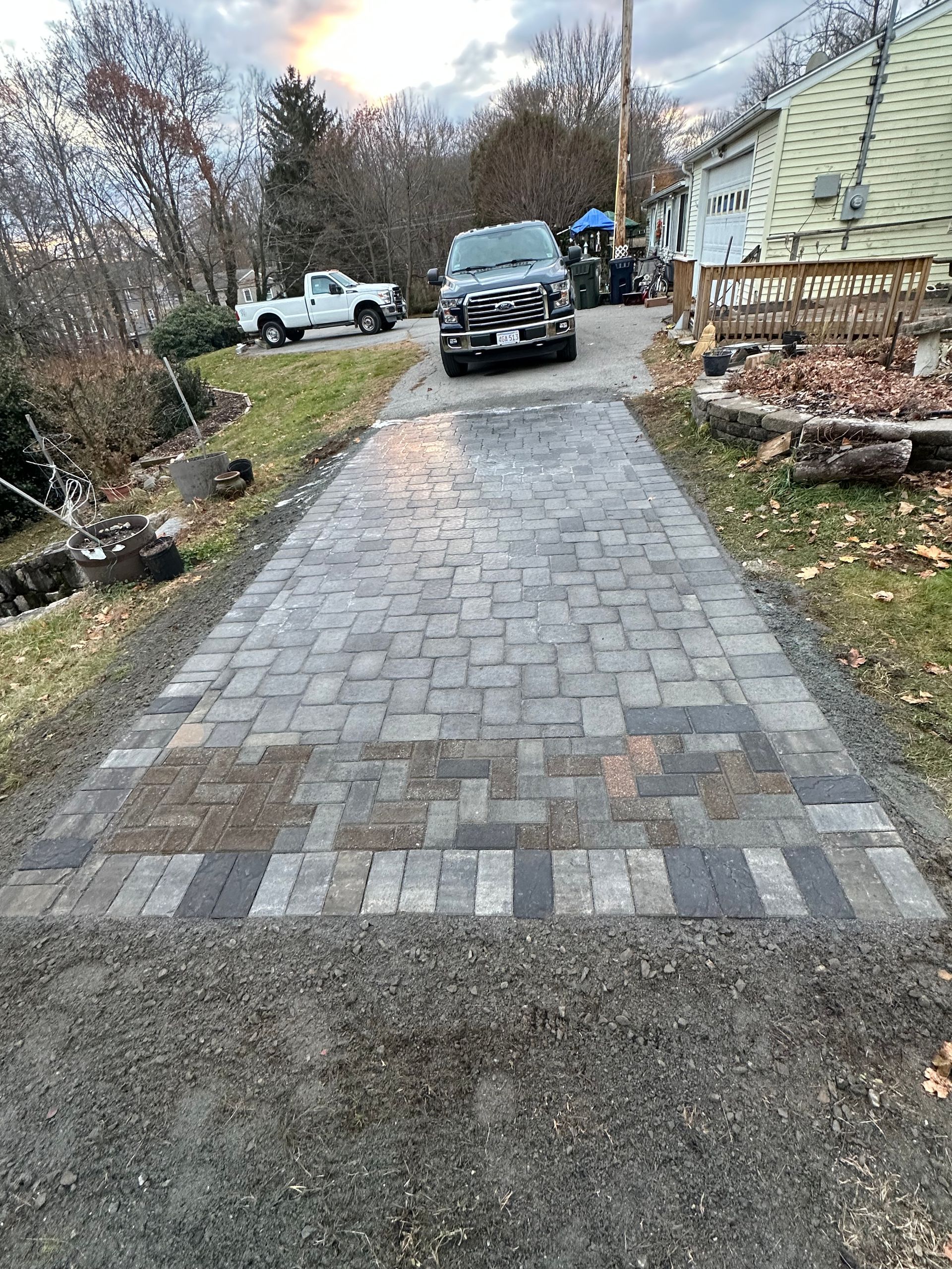 Brick driveway with a parked black SUV and a person standing near a house in a suburban yard