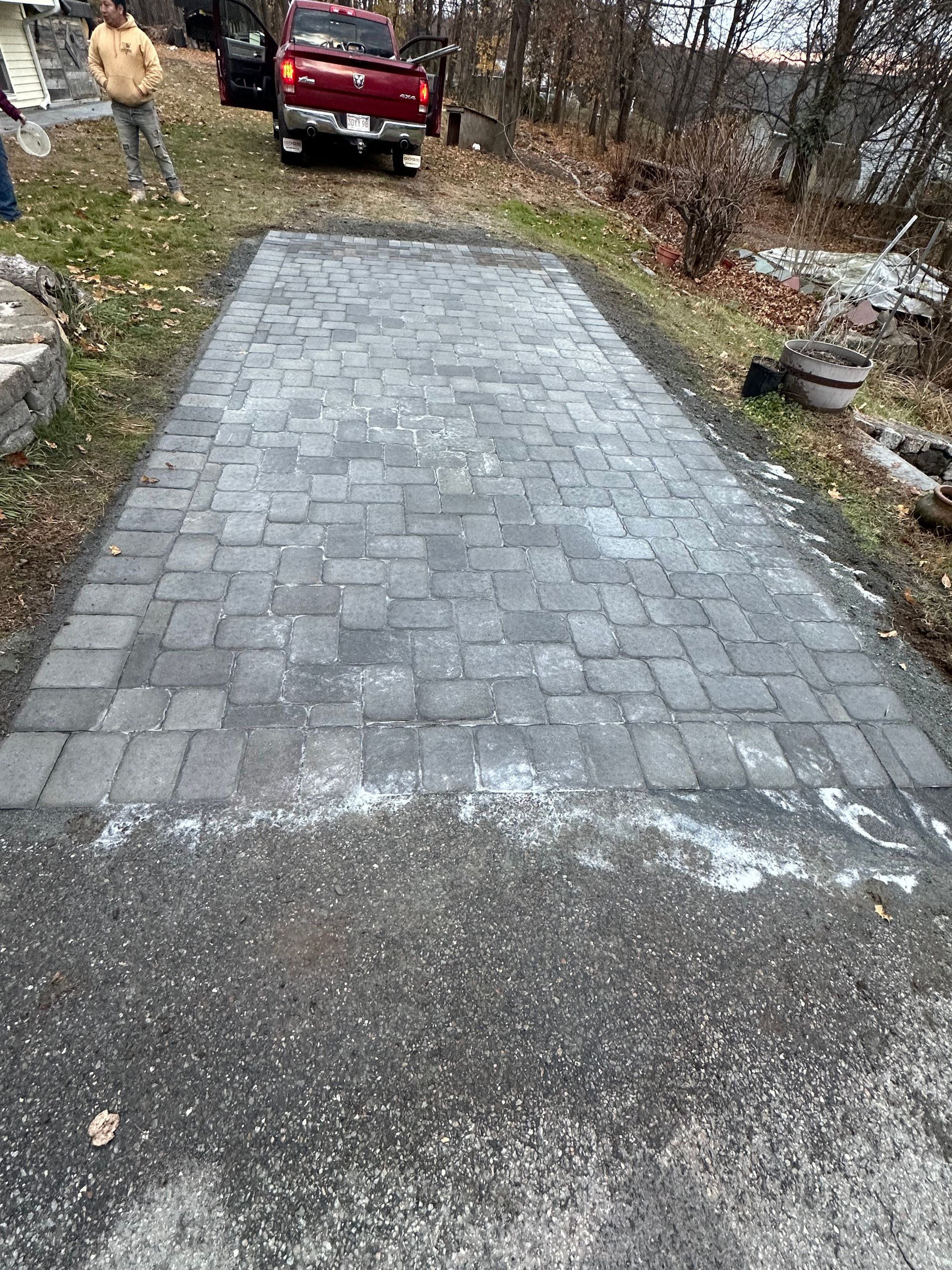 Stone-paver driveway leading to a red pickup truck in a wooded yard