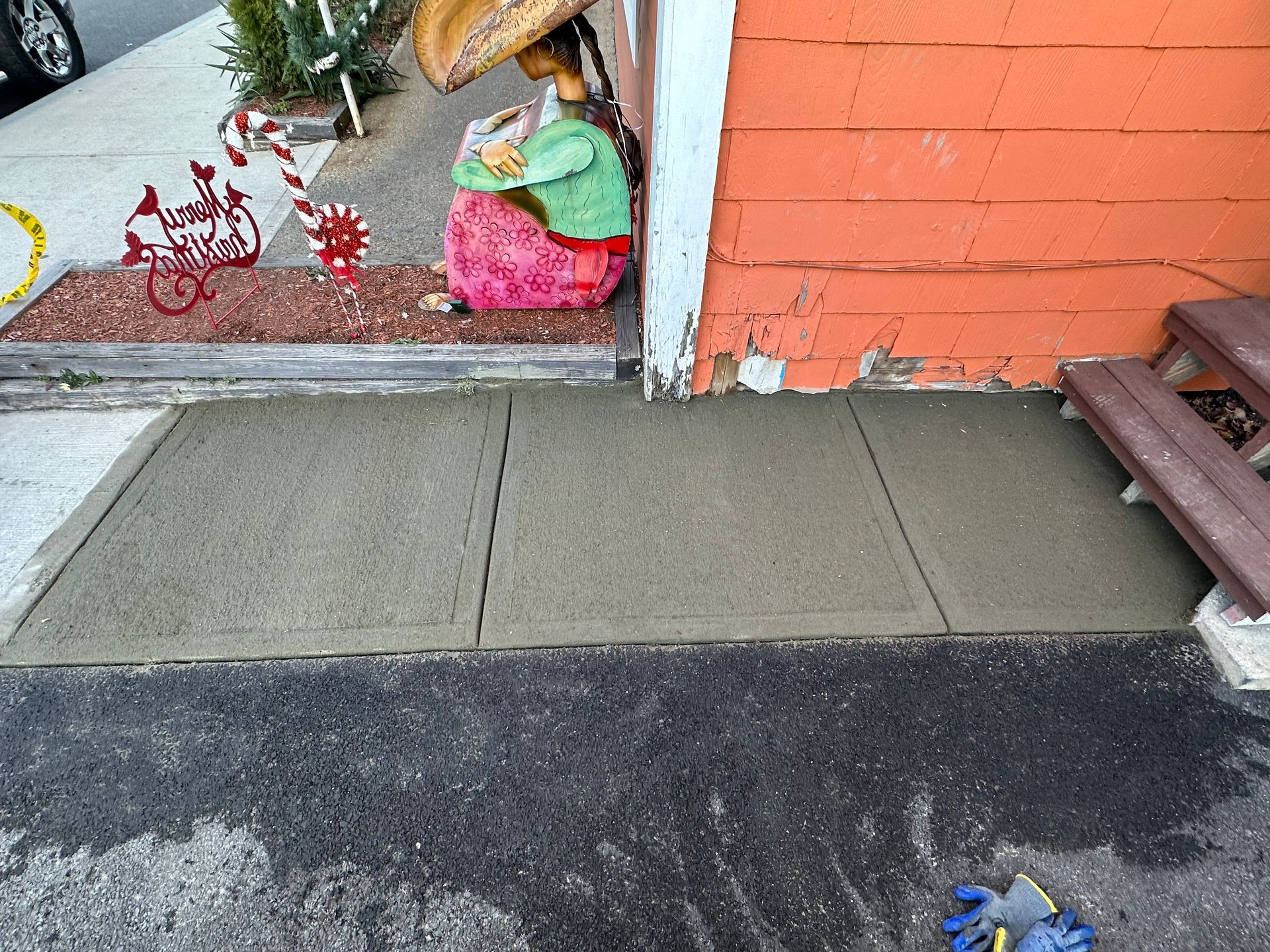 Sidewalk ramp beside an orange brick storefront with potted holiday decorations and a bench edge.